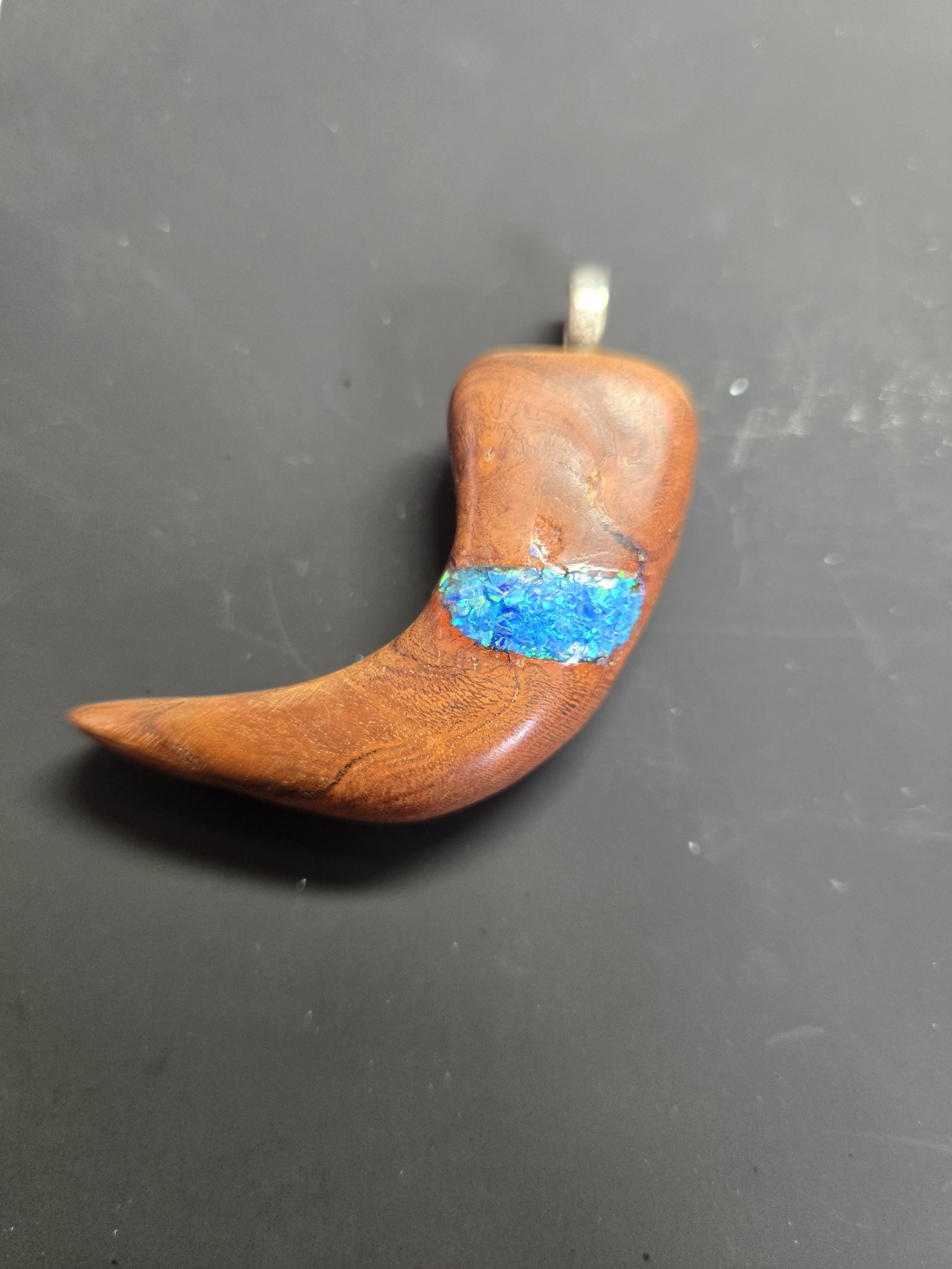 Front of a hand-carved maple bear claw pendant with a bright blue fire opal inlay band
