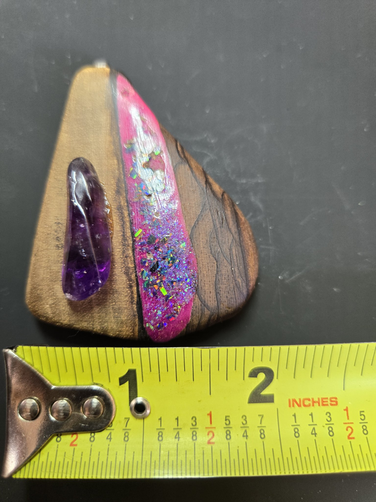 Front of a figured maple pendant beside a tape measure, with a pink crushed opal inlay band and teardrop amethyst stone