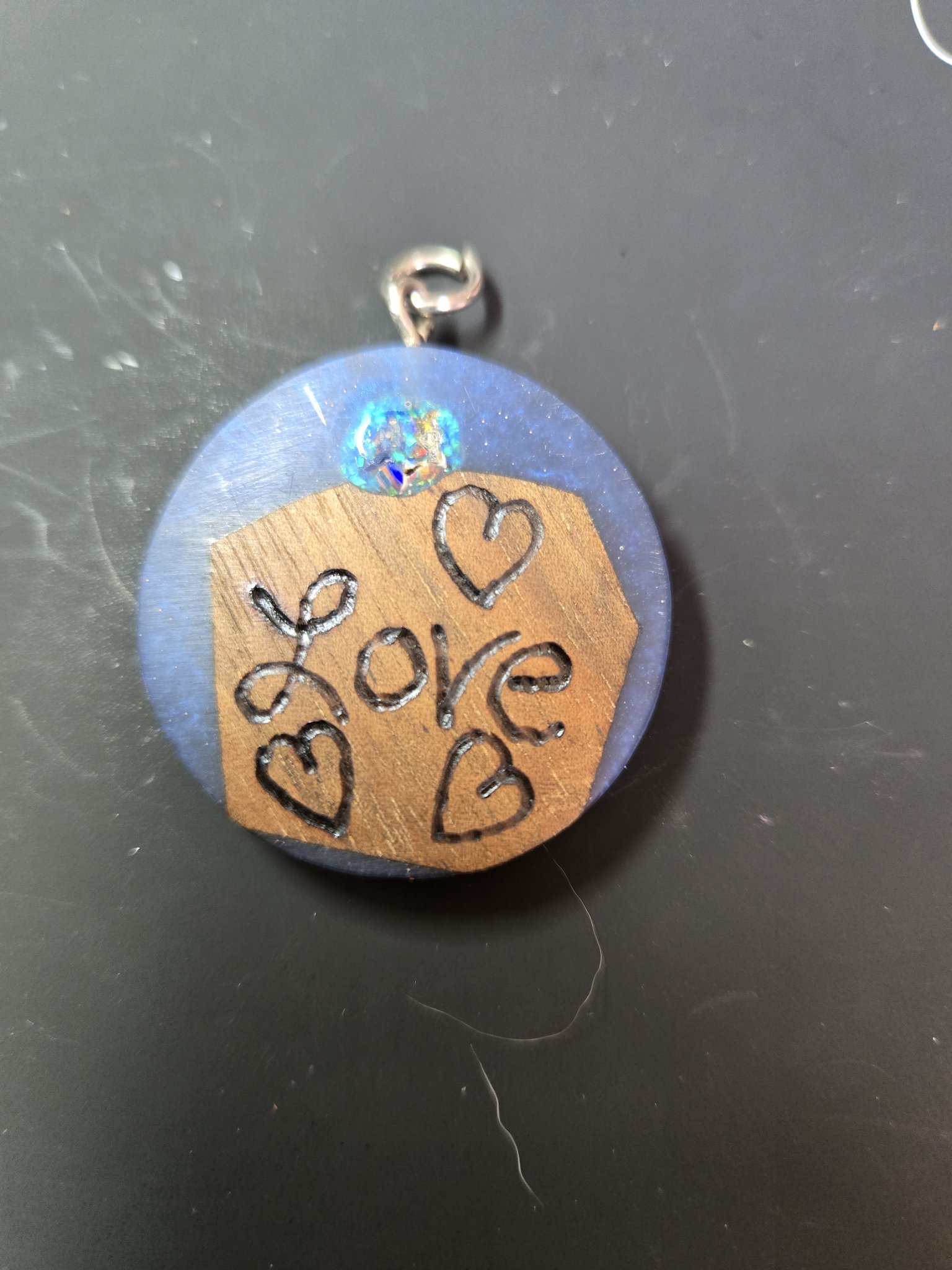 Front of a round blue resin and wood pendant with a fire opal cabochon and a wood-burned Love and hearts design