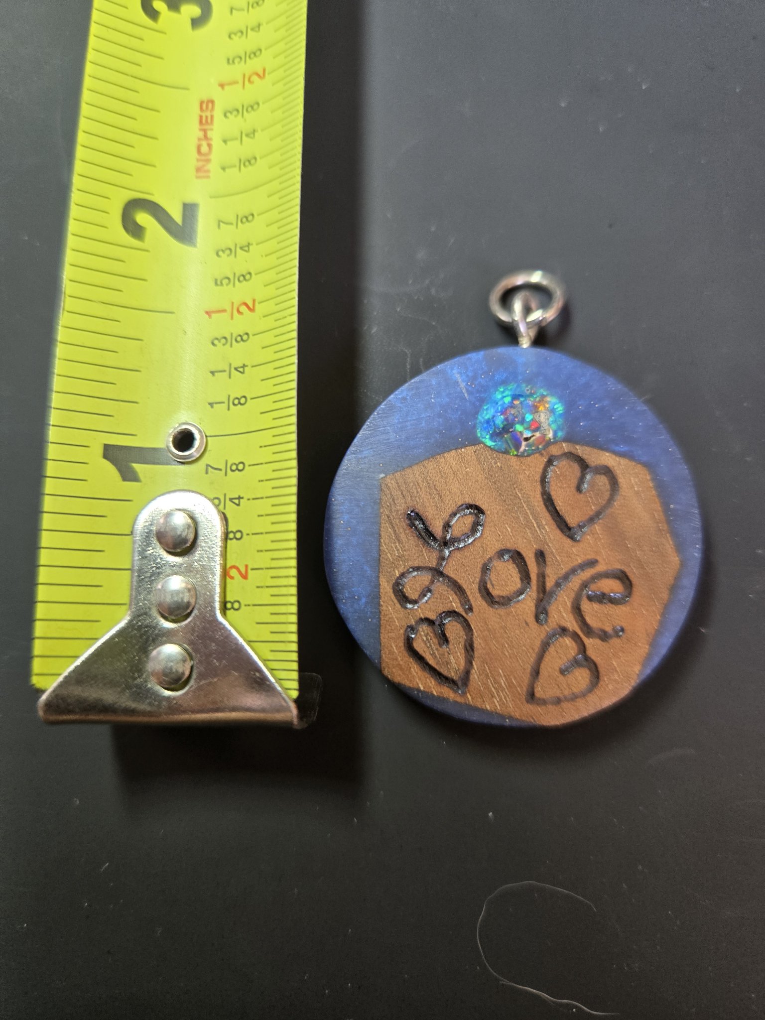 Love pendant beside a tape measure showing it is about two inches across