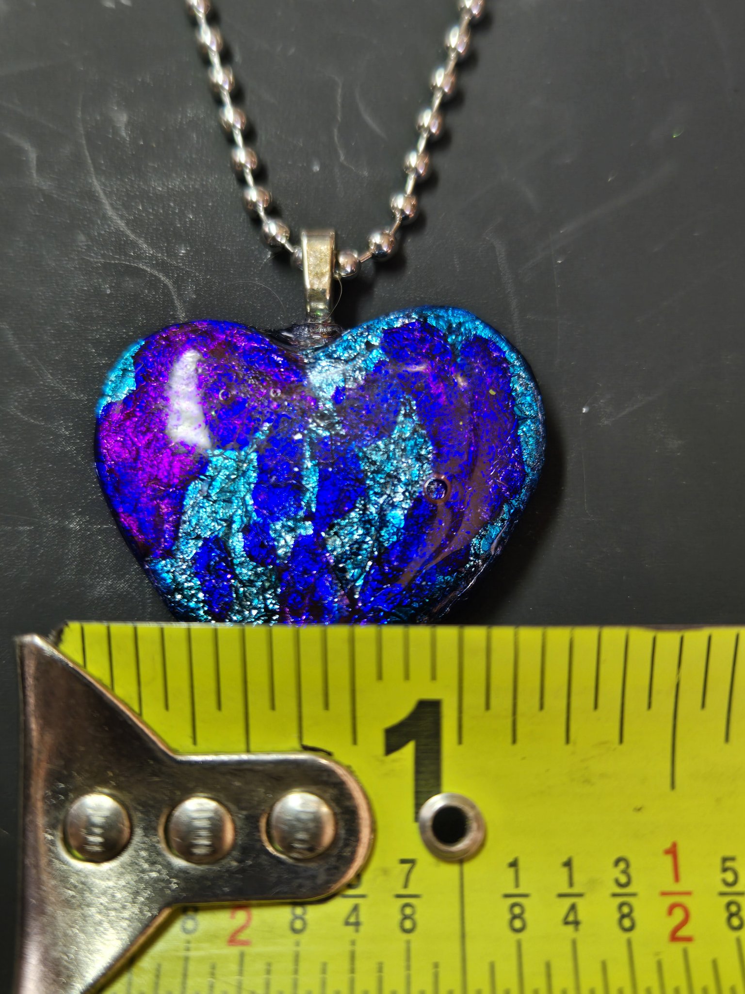 Alcohol ink heart pendant against a tape measure showing it is about one and a half inches wide
