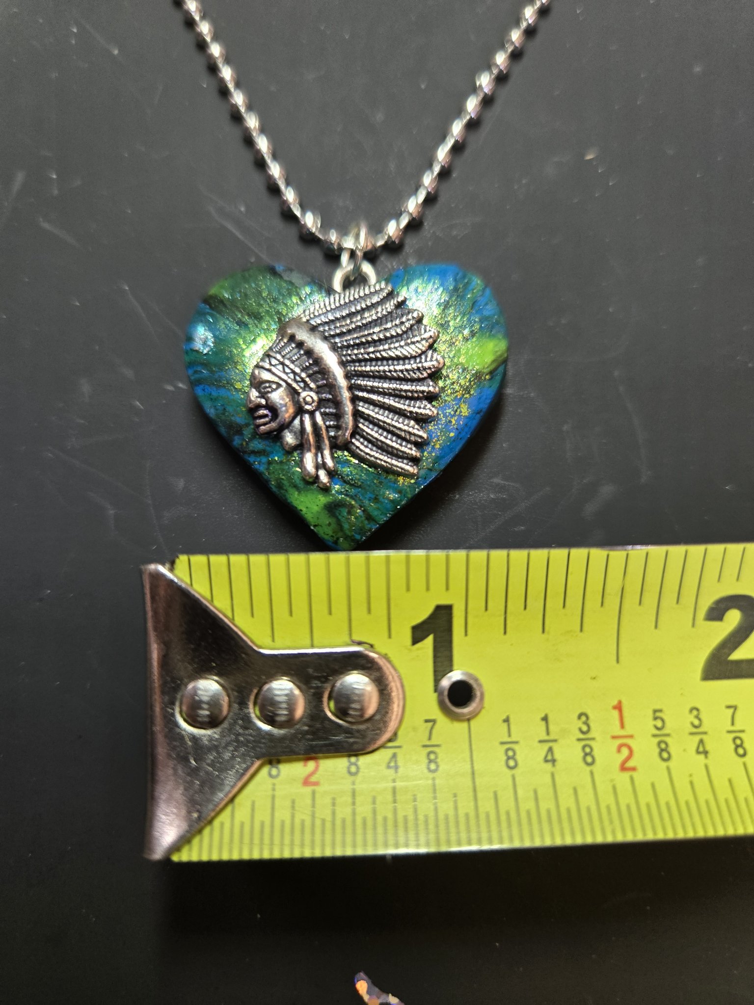 Headdress heart pendant against a tape measure showing it is about one and a half inches wide