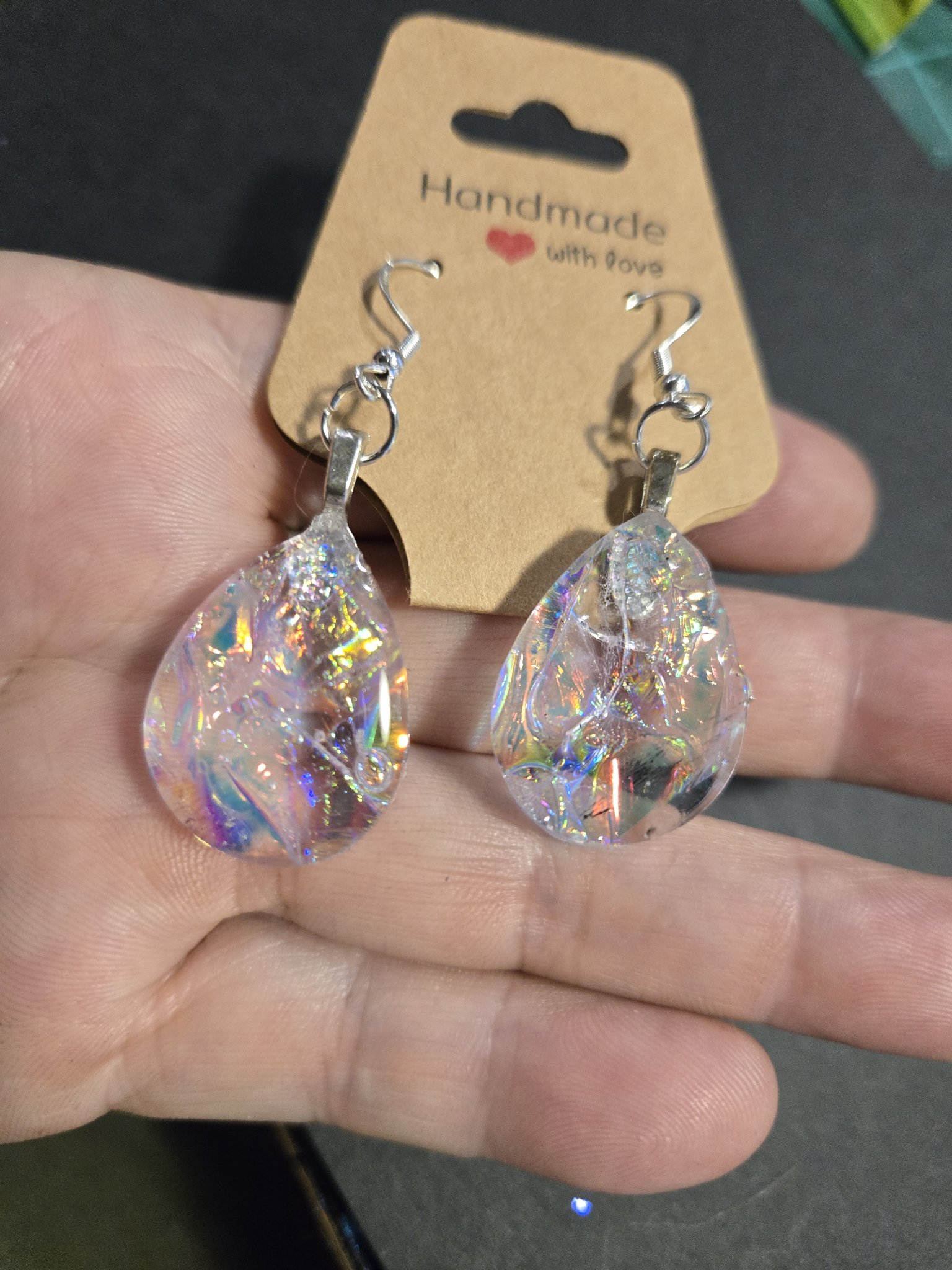 Holographic acrylic teardrop earrings held in a hand, showing their rainbow finish and sterling silver ear wires