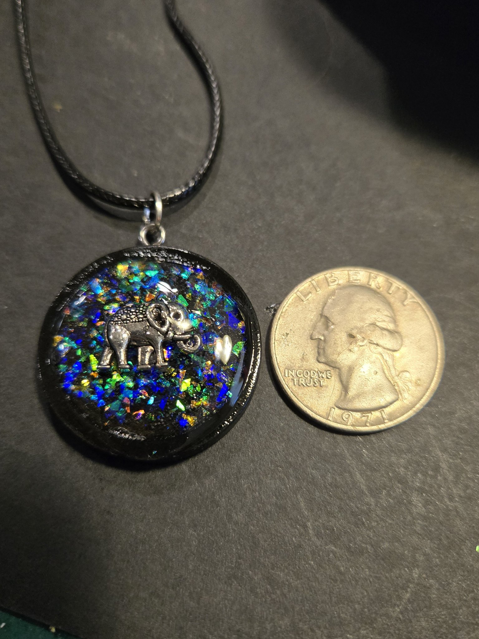 Holographic elephant pendant beside a quarter showing it is slightly larger and about one and a half inches across