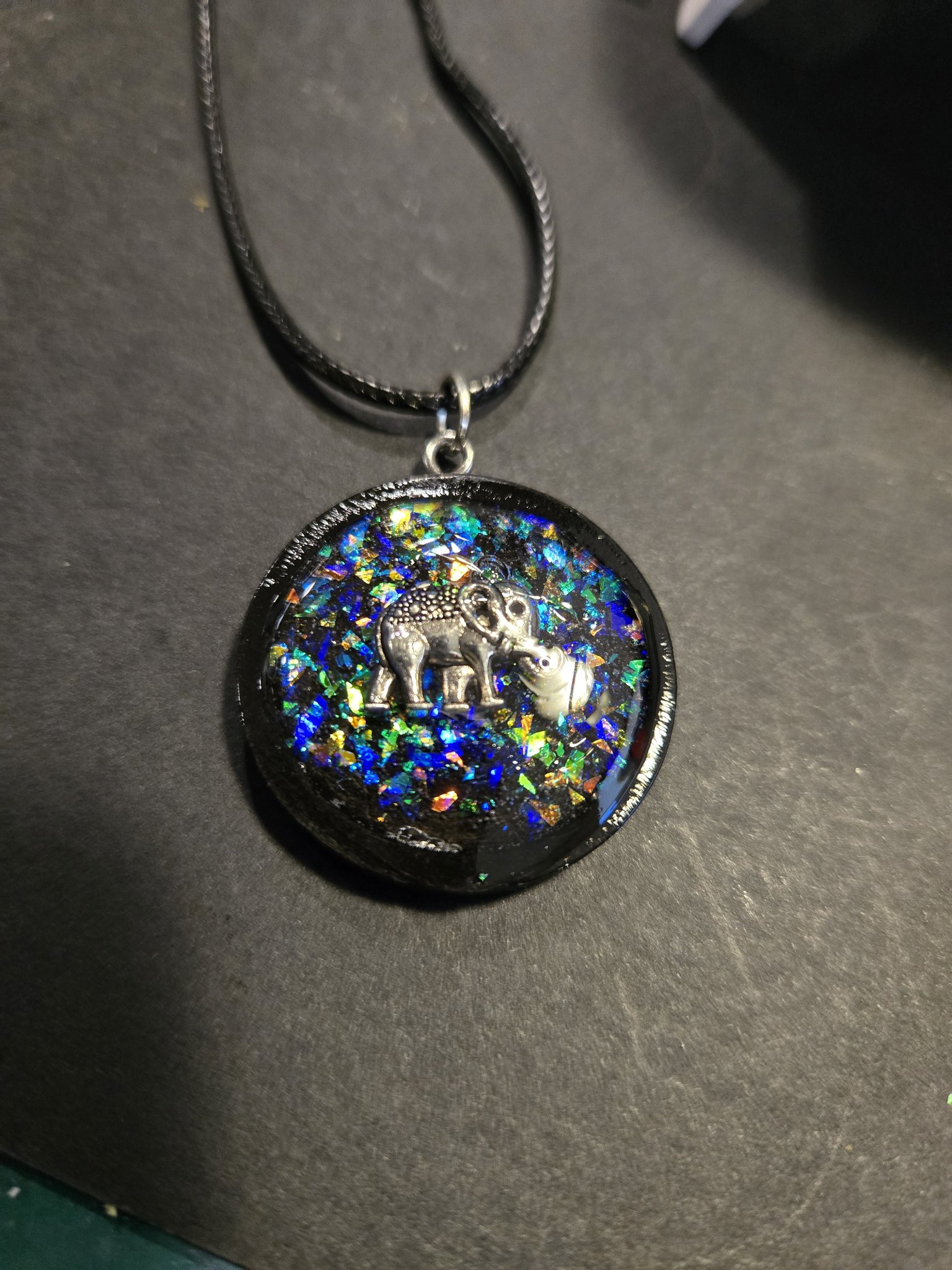 Holographic elephant pendant and black necklace displayed on a dark background