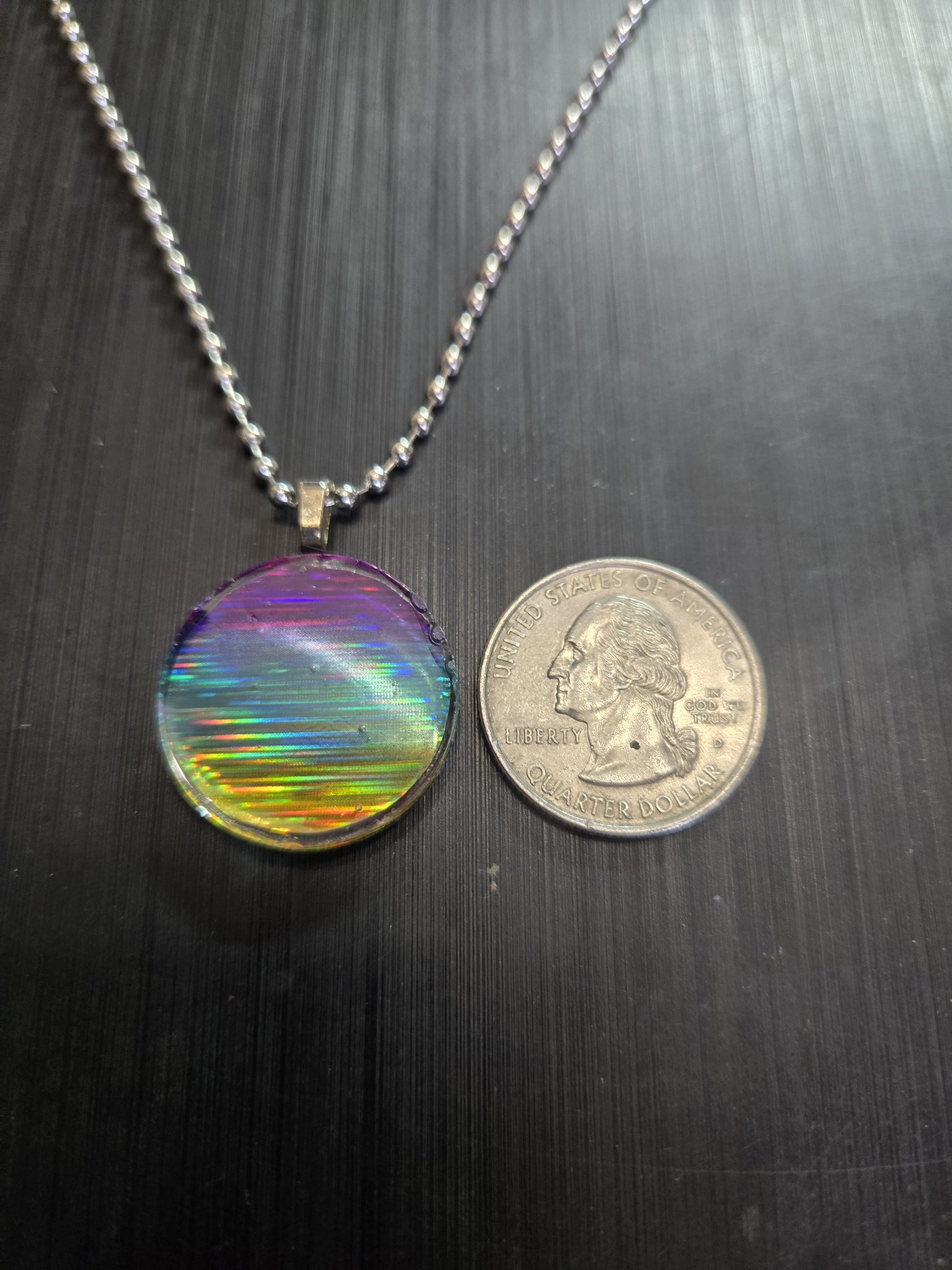 Front of the holographic rainbow pendant beside a quarter showing it is approximately one and a half inches across