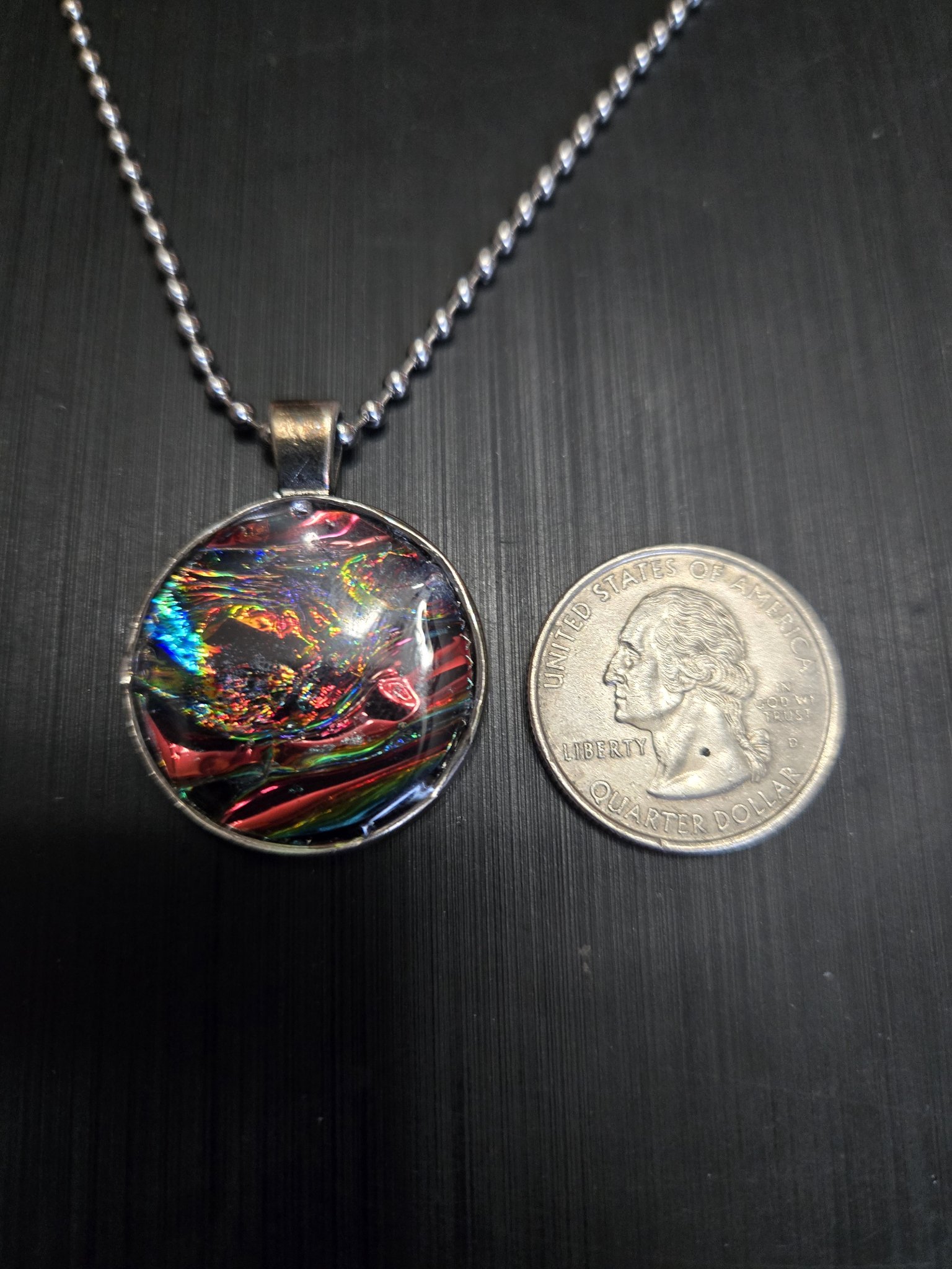 Front of the dark rainbow holographic pendant beside a quarter showing it is approximately one and a half inches across