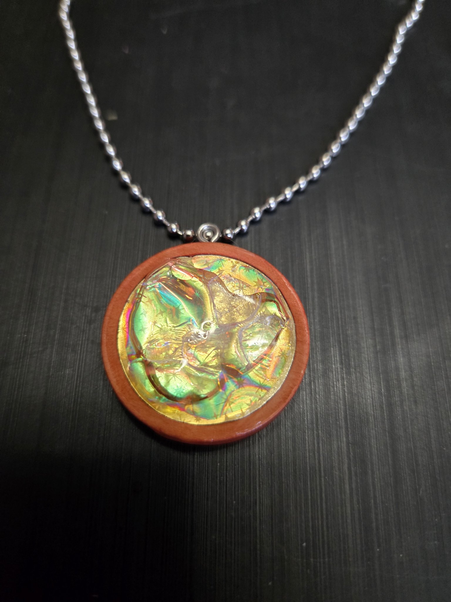 Front view of the round wood pendant with golden-green holographic resin inlay on its 22-inch ball chain