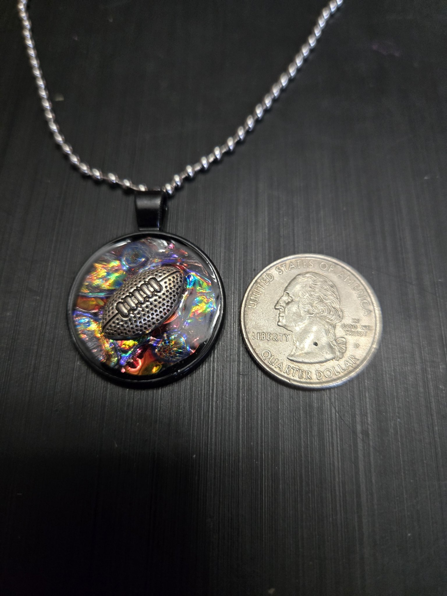 Front of the holographic football pendant beside a quarter showing it is approximately one and a half inches across