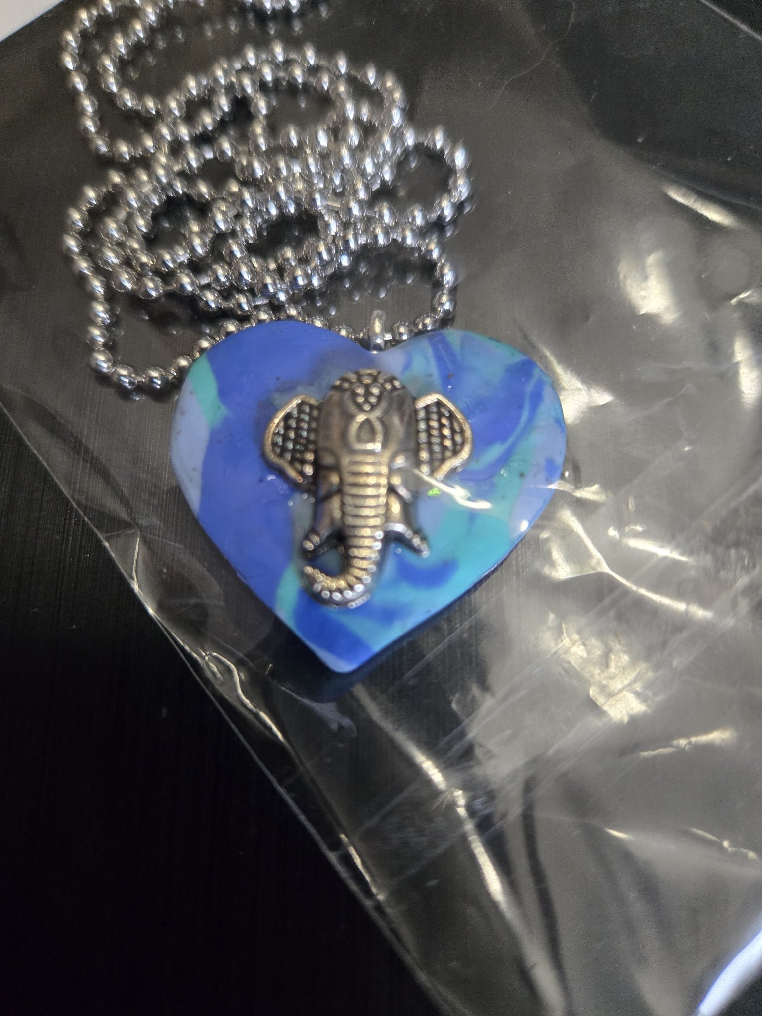 Front close-up of the blue and teal swirl polymer clay heart pendant with a silver-tone elephant charm on its 22-inch ball chain