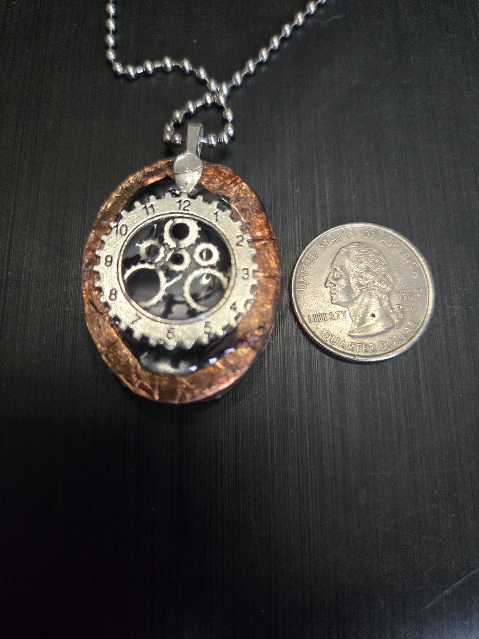 Steampunk back of the double-sided pendant with silver-tone gears and clock face details beside a quarter