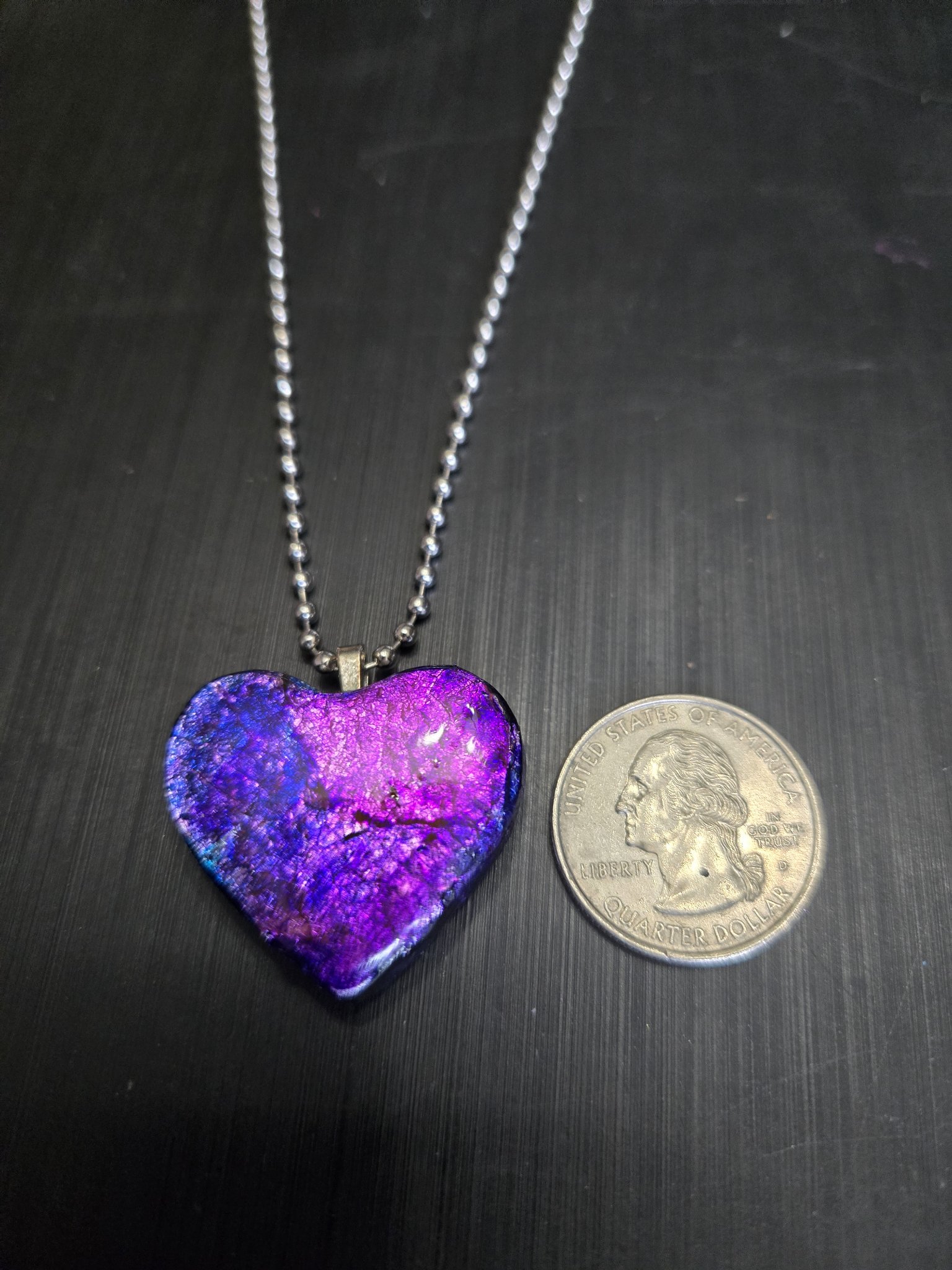 Front of the purple, blue, and pink heart pendant beside a quarter showing it is approximately two inches across