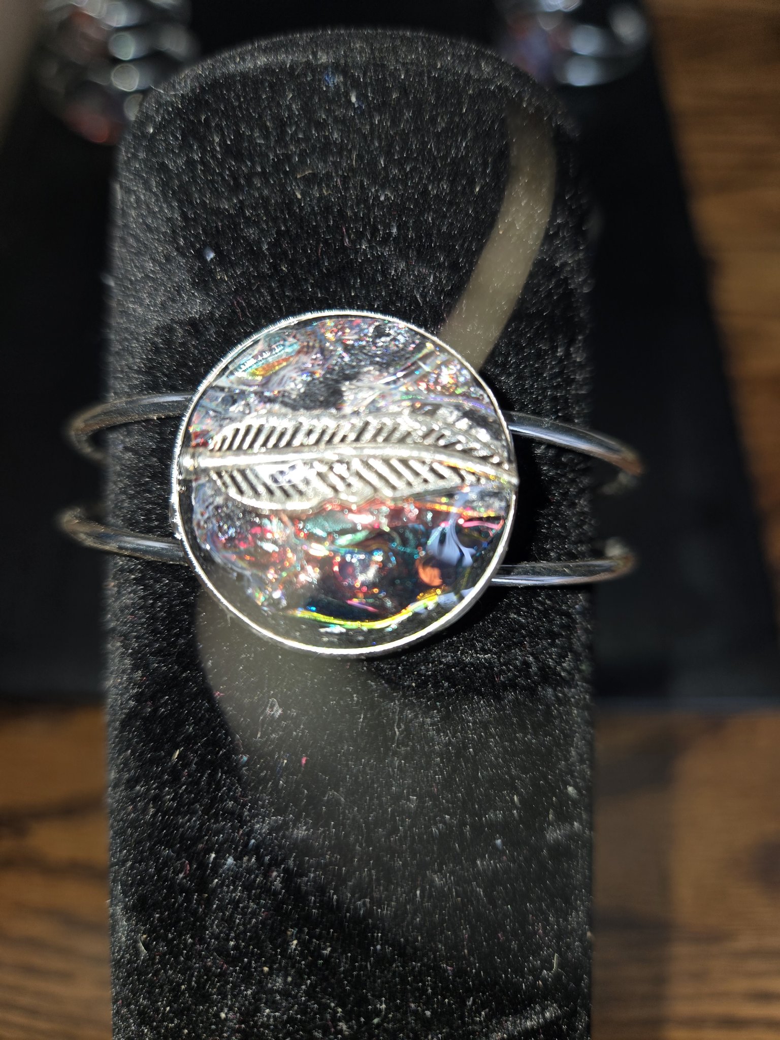 Alternate close-up of the silver-tone cuff bracelet and feather medallion on a black display stand