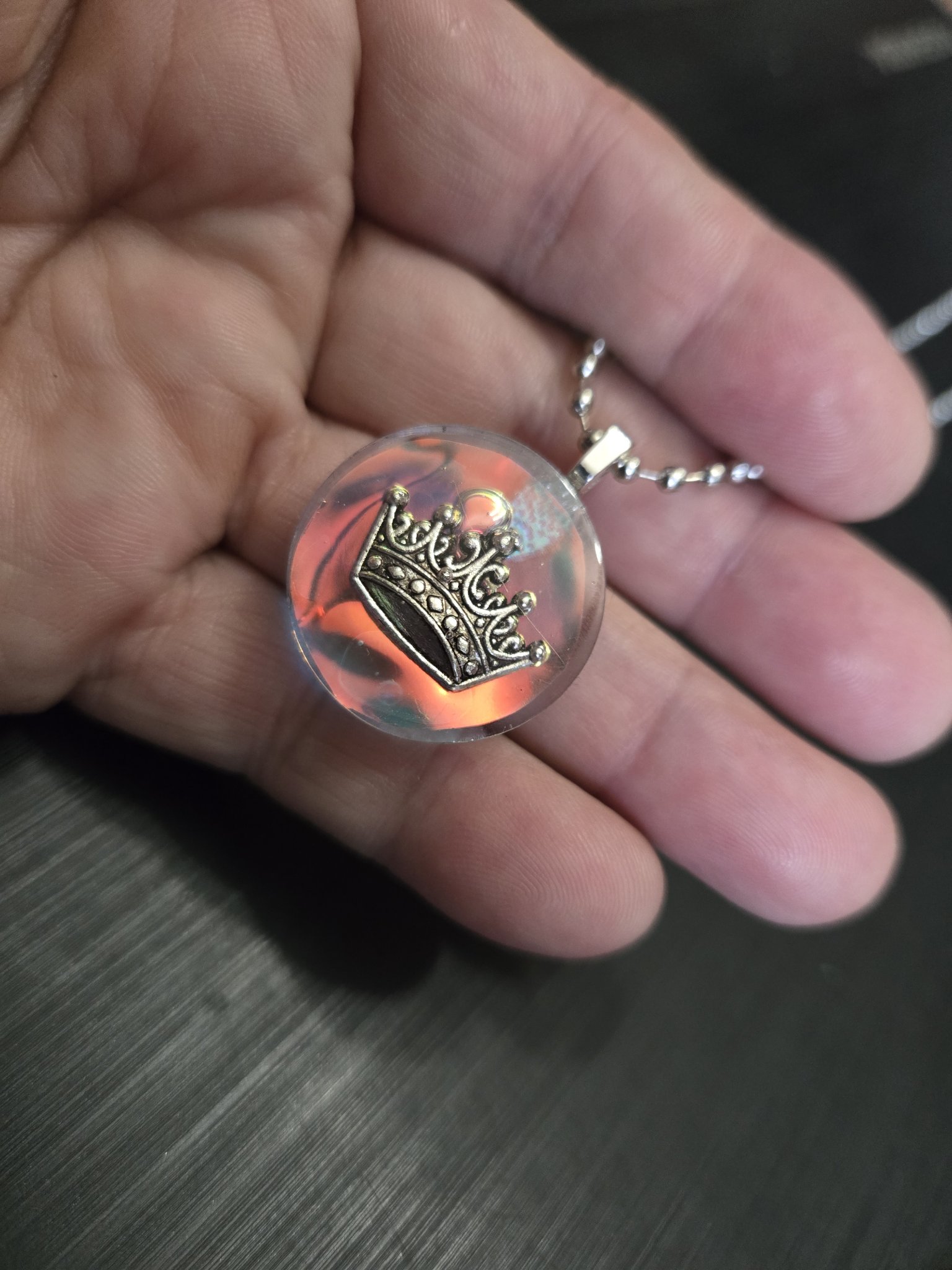 Stock 146 holographic resin crown pendant held in a hand, showing its orange-red iridescent color shift