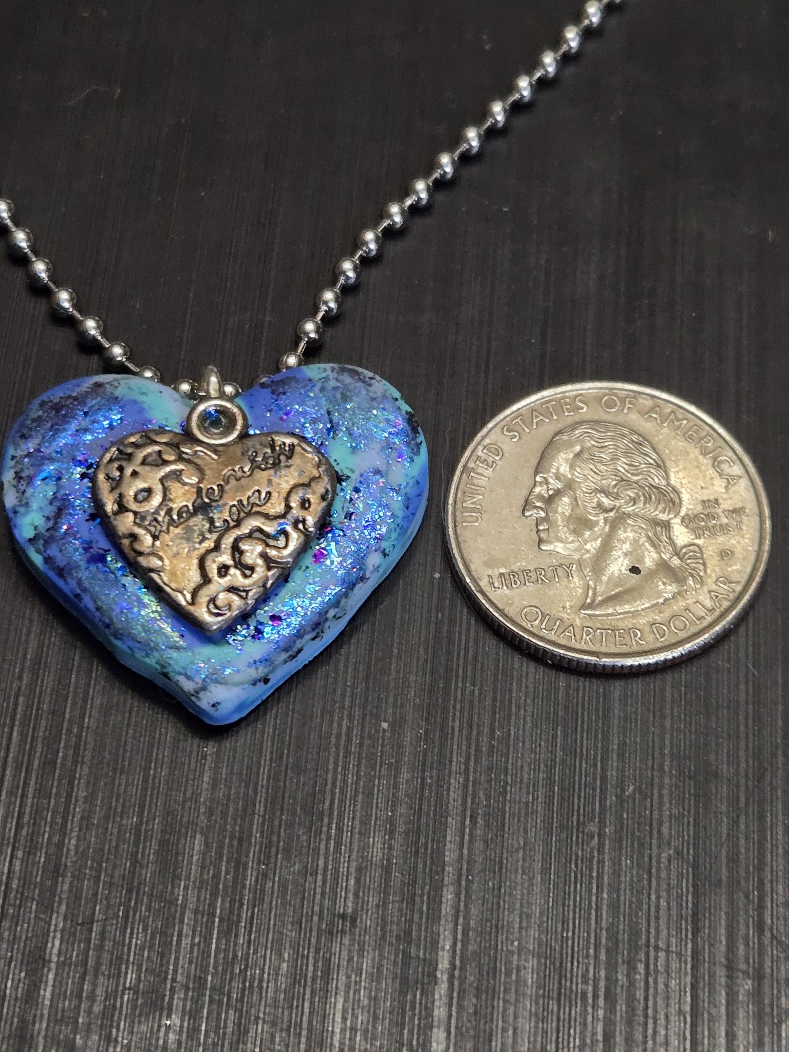 Stock 152 blue iridescent heart pendant beside a quarter showing it is approximately two inches across