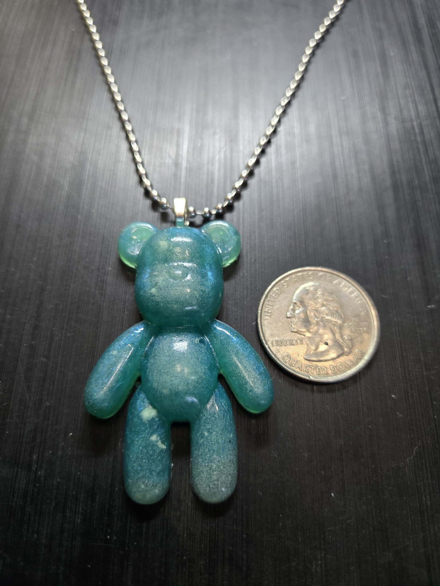 Stock 155 glow-in-the-dark resin teddy bear pendant beside a quarter showing it is approximately two inches tall