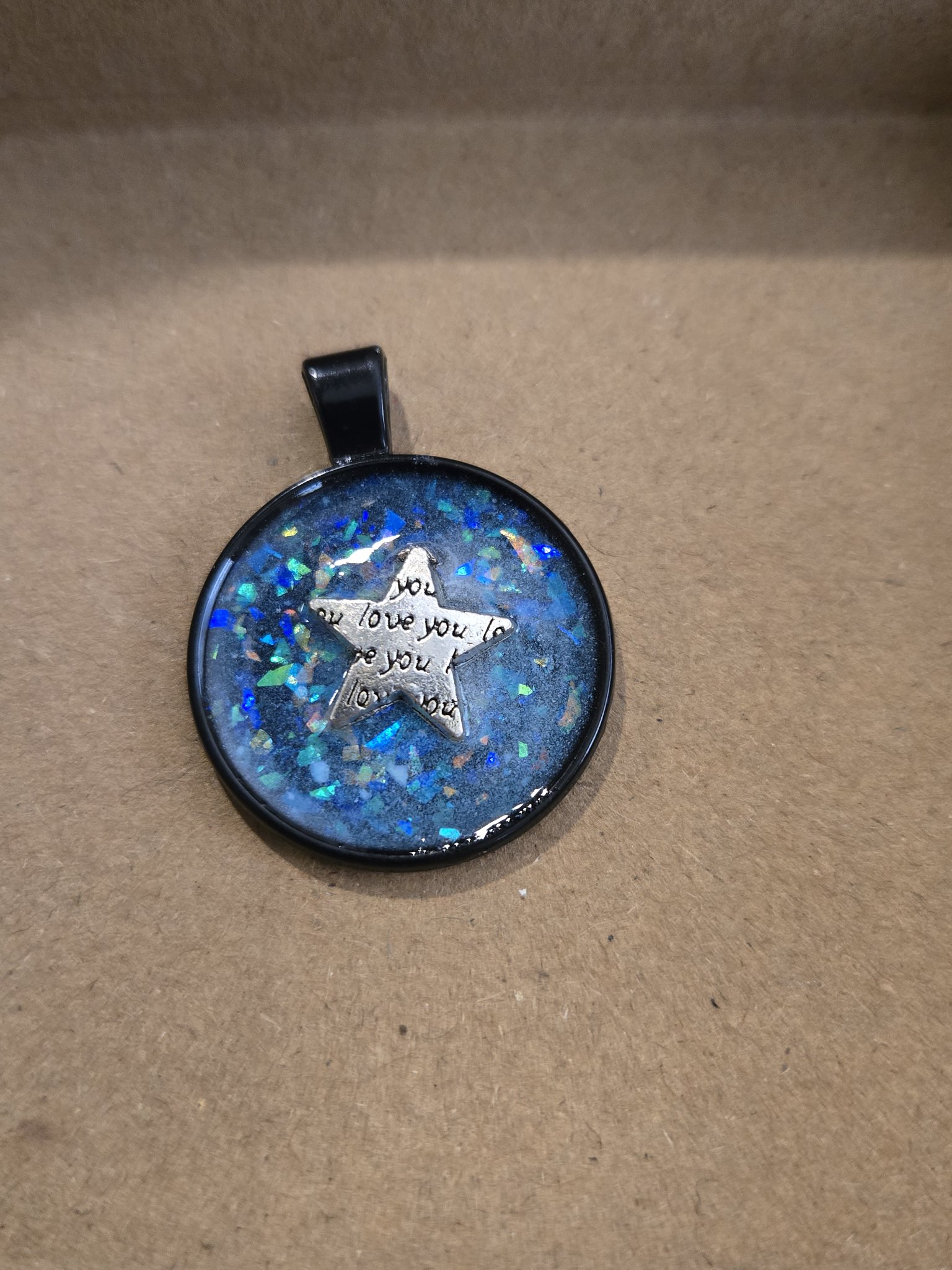 Alternate angle of stock 169 showing the blue holographic glitter resin, black metal frame, and love you star charm
