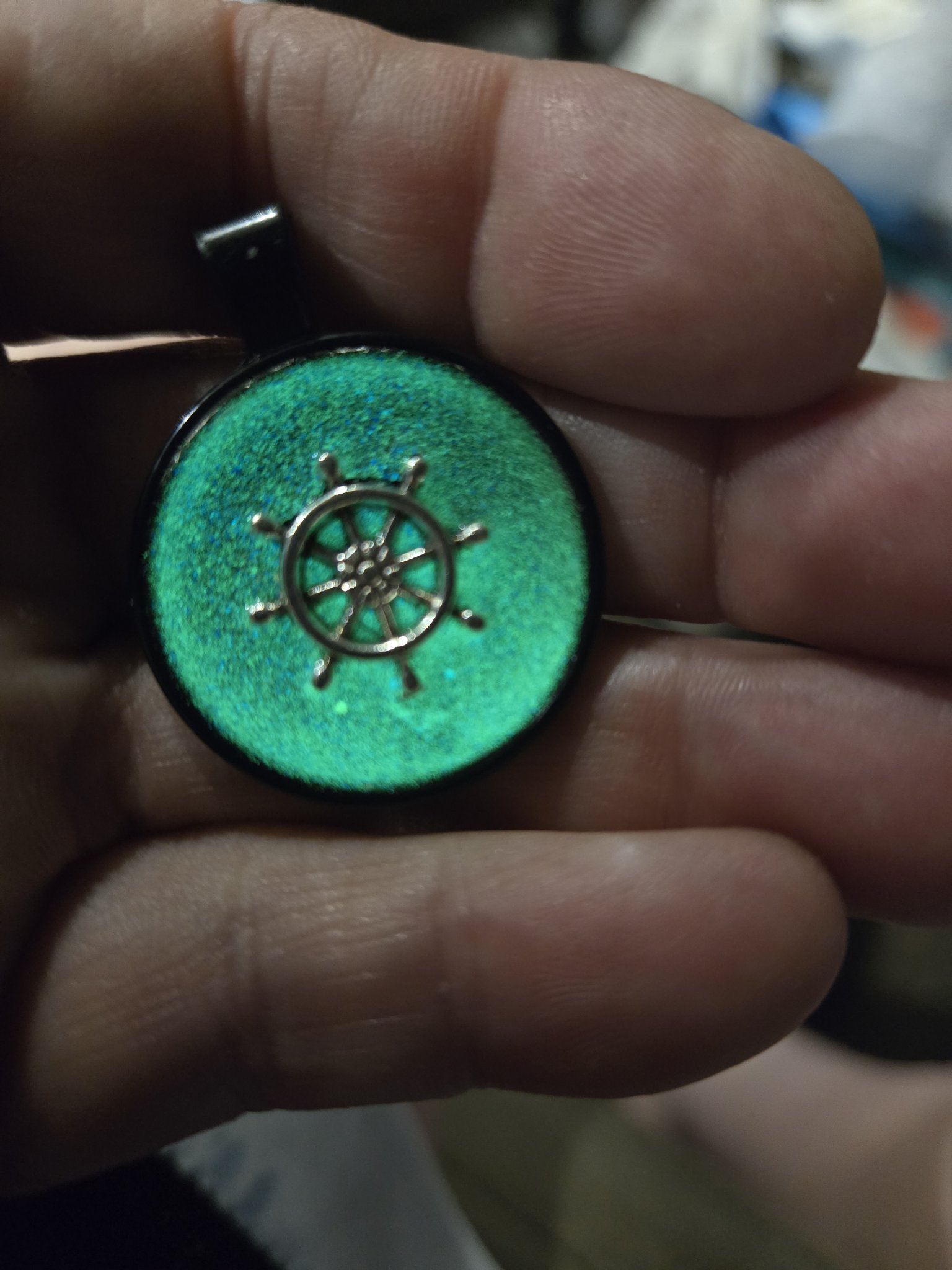 Stock 195 ship's wheel resin pendant glowing green in the dark while held in a hand