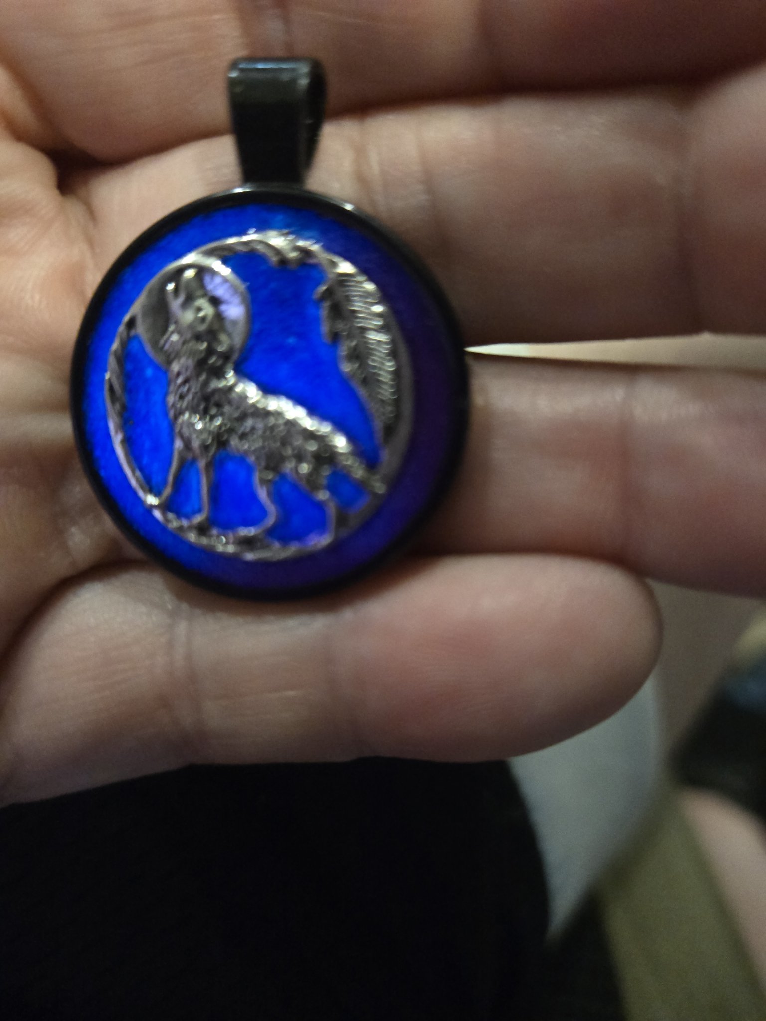 Stock 198 round glow-in-the-dark howling wolf resin pendant in a black metal frame, shown from the front in a hand