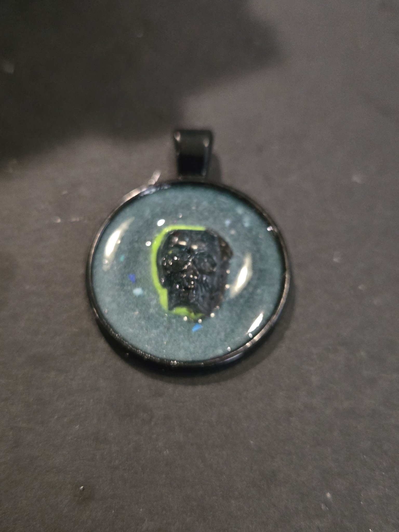 Stock 199 round glow-in-the-dark crystal skull resin pendant in a black metal frame, shown from the front
