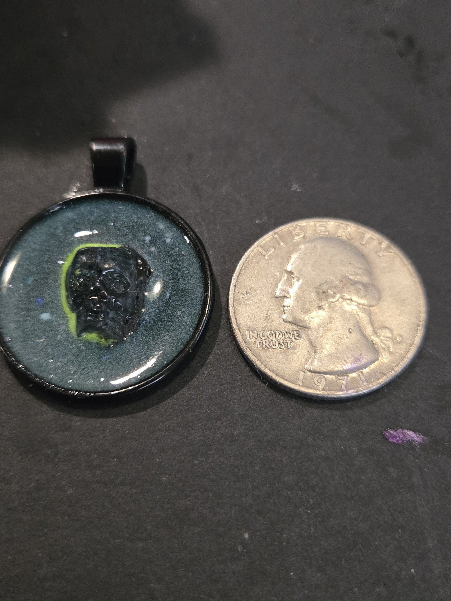 Front of stock 199 crystal skull resin pendant beside a quarter for scale