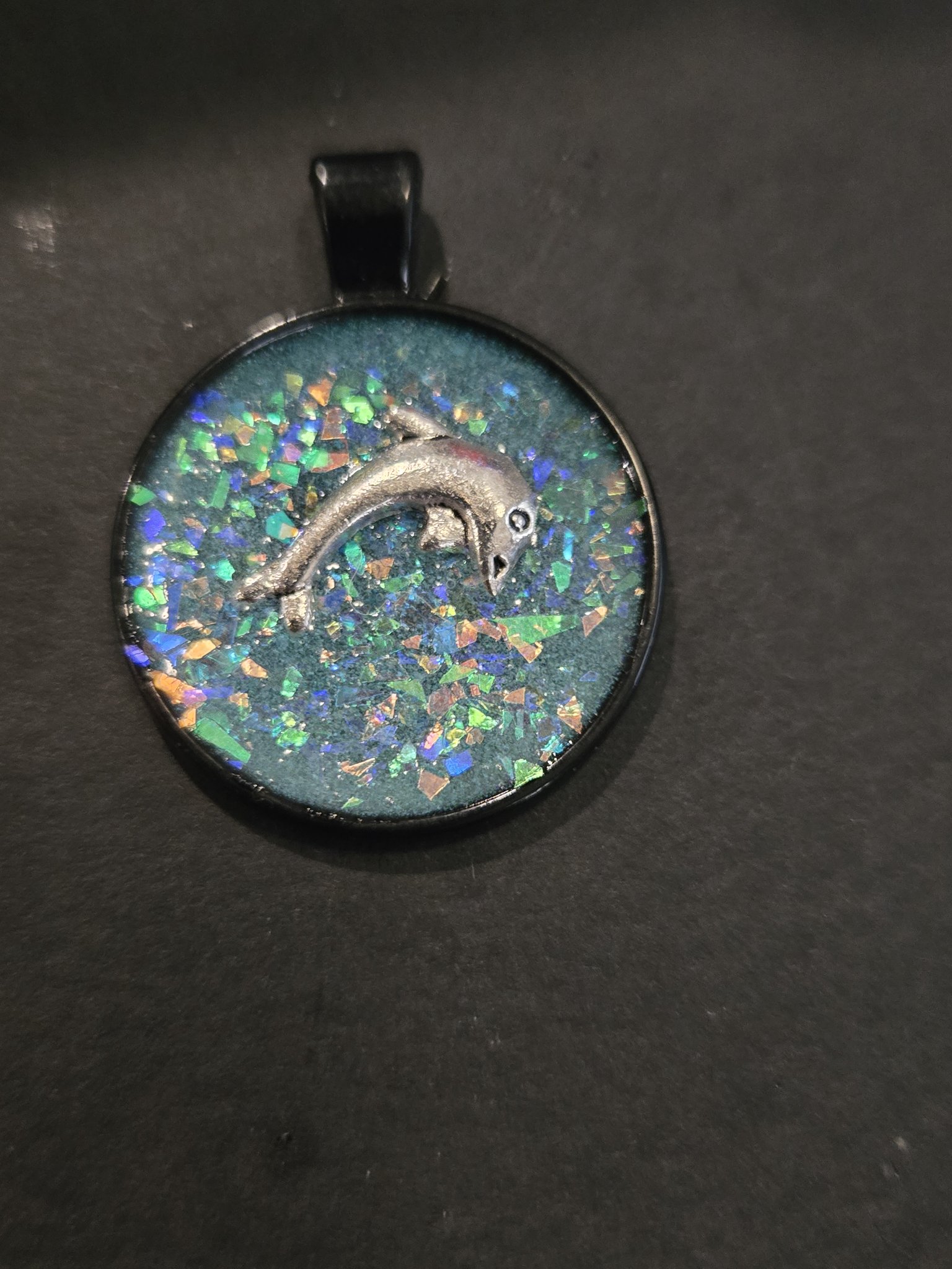 Stock 201 round blue glow-in-the-dark dolphin resin pendant in a black metal frame, shown from the front