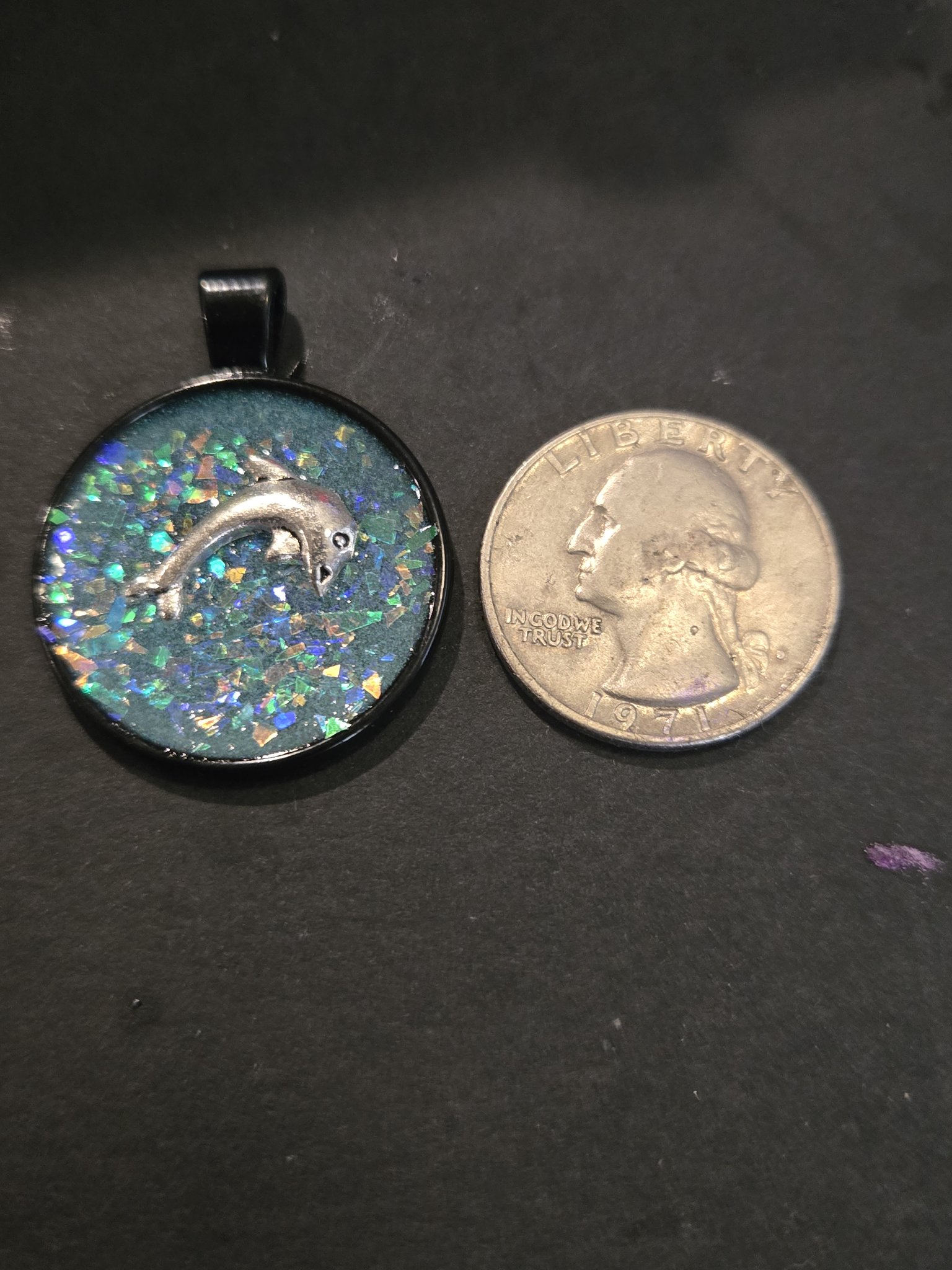 Front of stock 201 dolphin resin pendant beside a quarter for scale