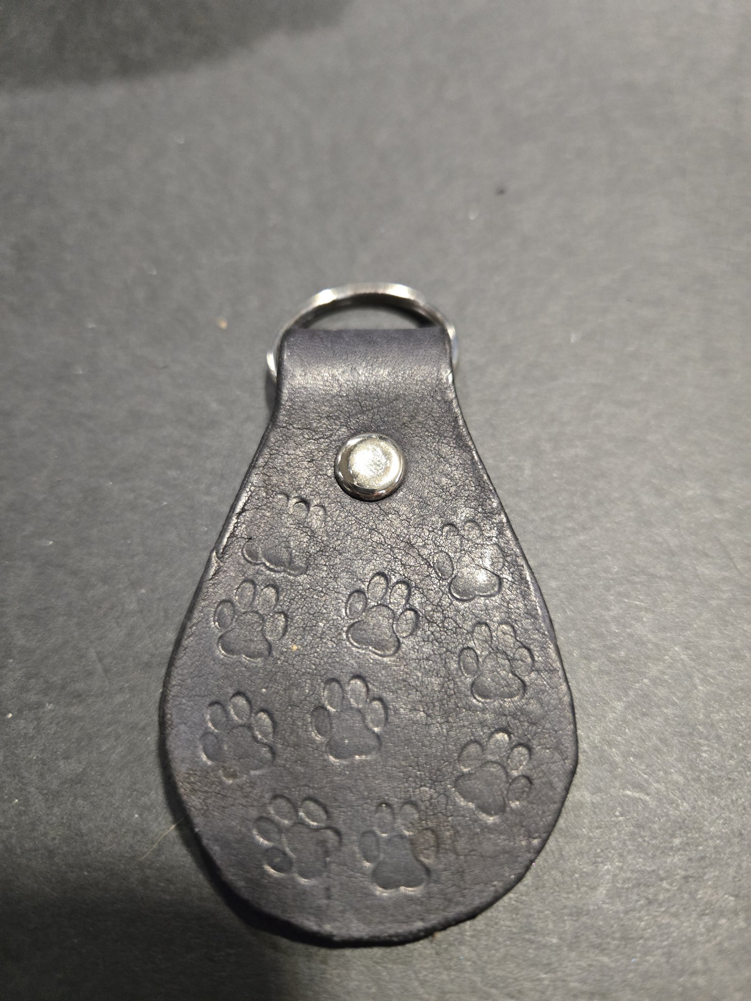 Stock 241 black leather keychain hand-stamped with dog paw prints all over, shown with its silver-tone rivet and split key ring