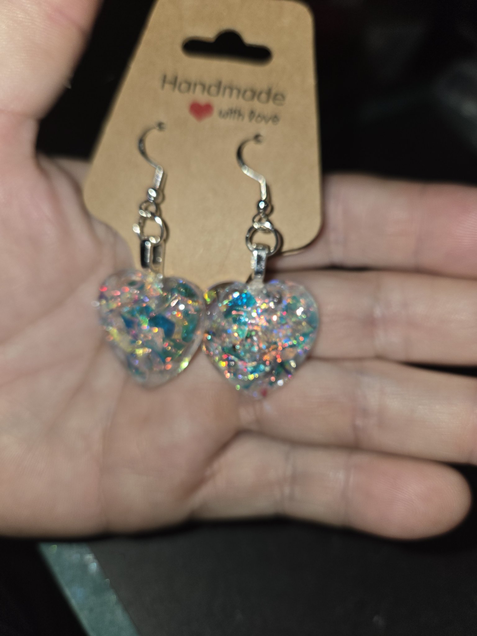 Stock 246 holographic heart earrings held in a hand for scale, showing their size and feather-light look