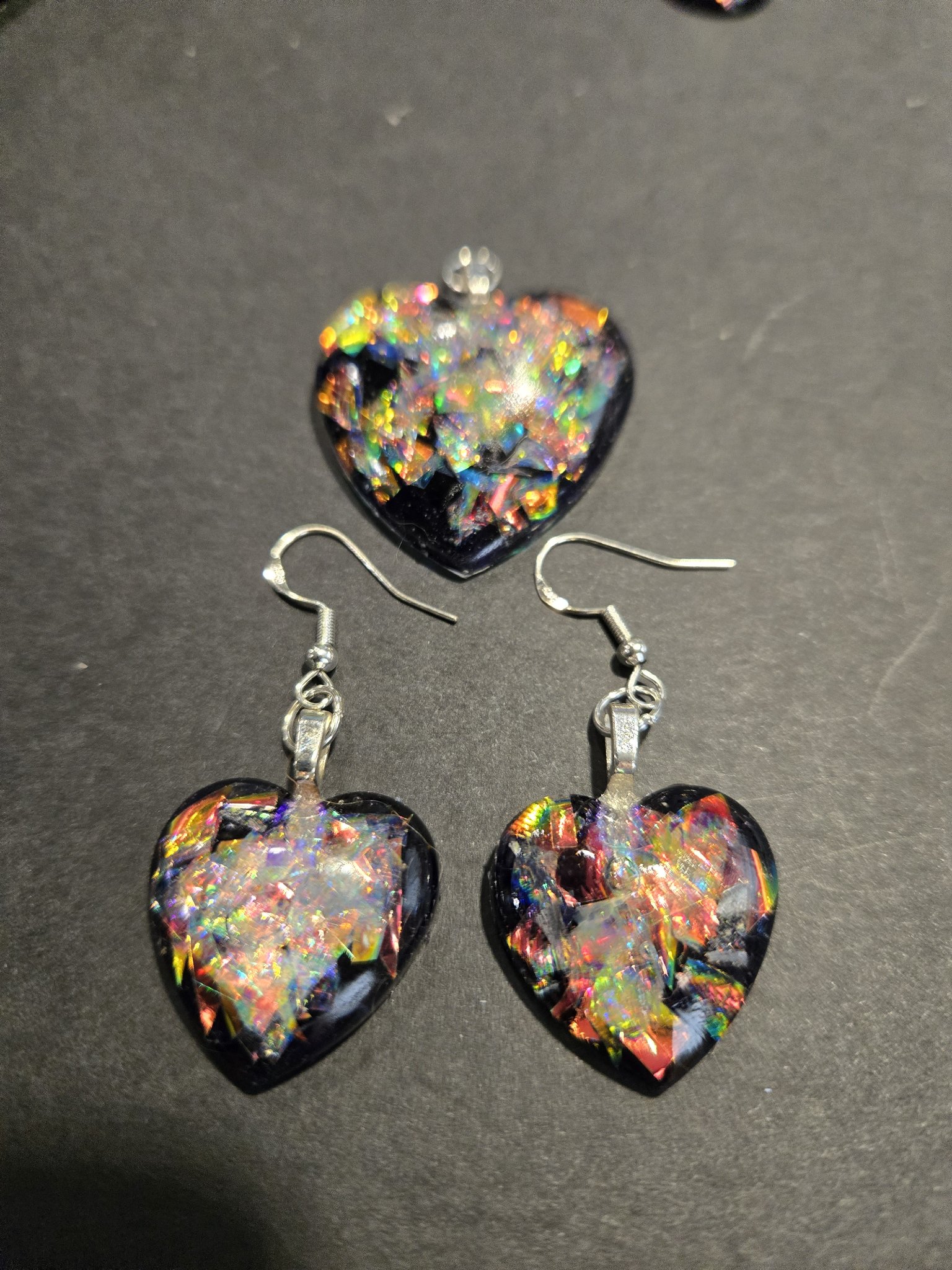 Stock 248 holographic heart earrings and pendant set — black resin hearts filled with rainbow holographic flakes, the pendant above the matching earrings on sterling silver wires