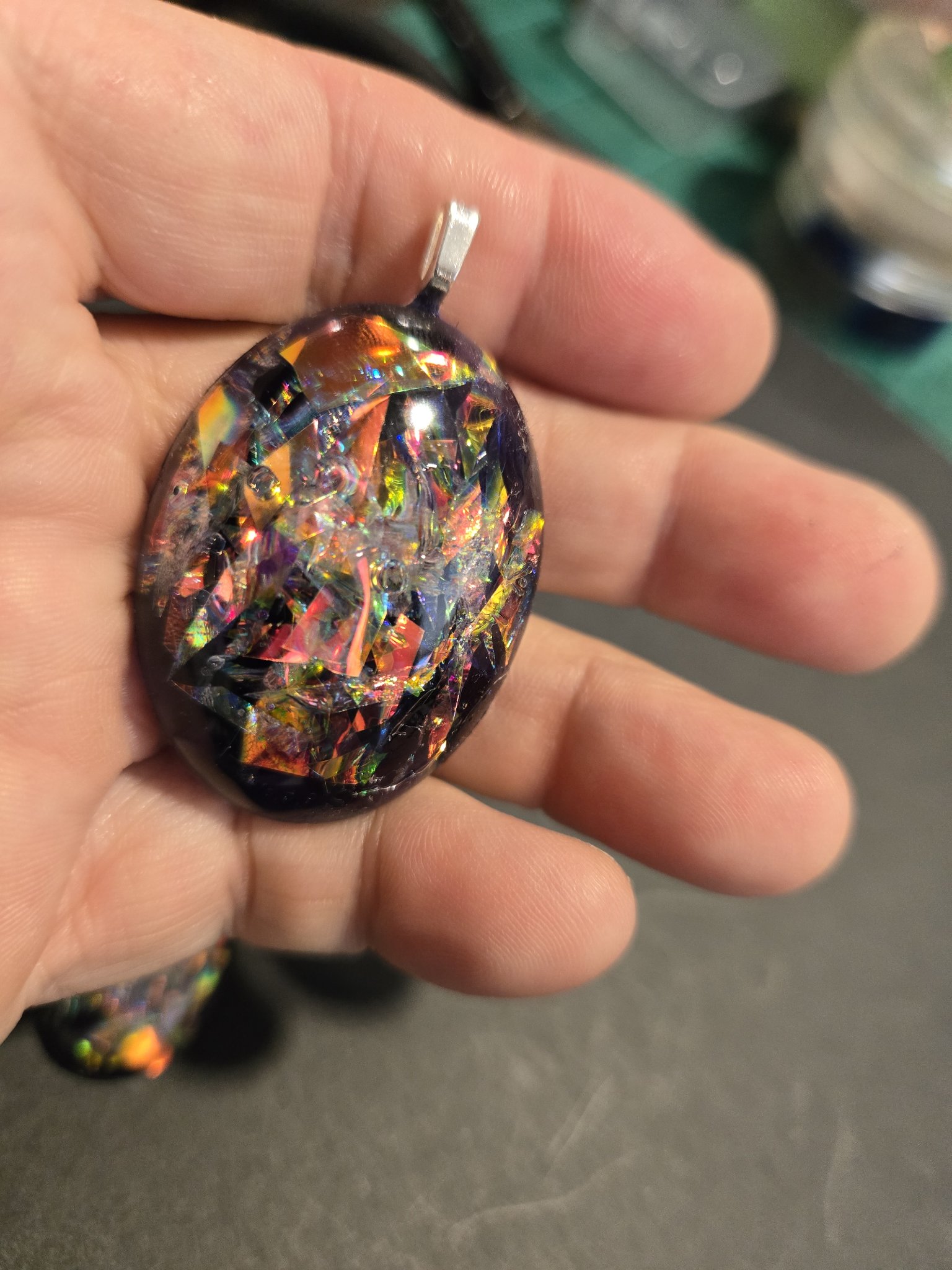 Stock 249 holographic oval pendant held in a hand, showing its size and the rainbow holographic flakes against the black resin