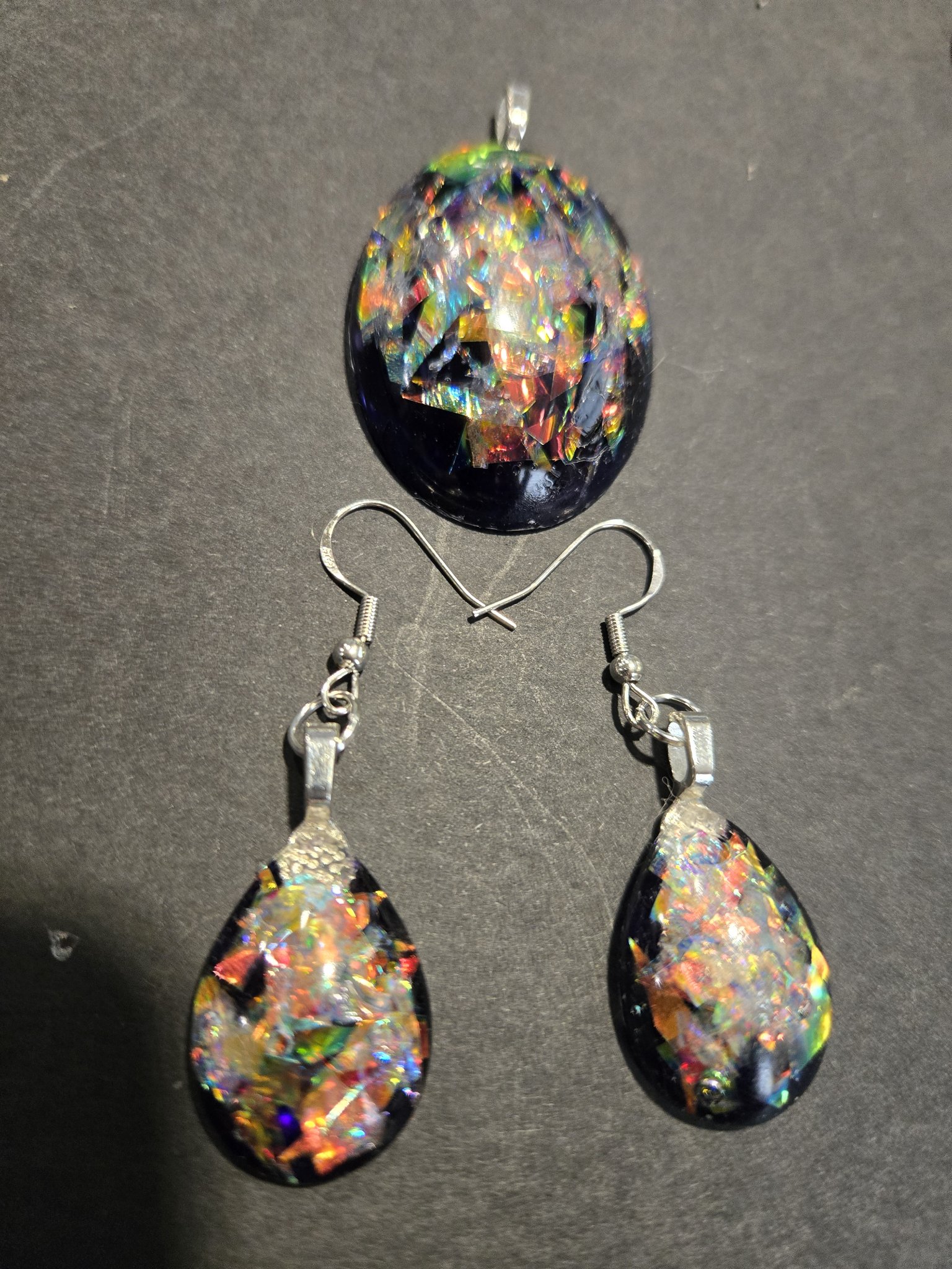 Another view of the stock 249 holographic teardrop earrings and oval pendant set, the pieces flashing rainbow colors