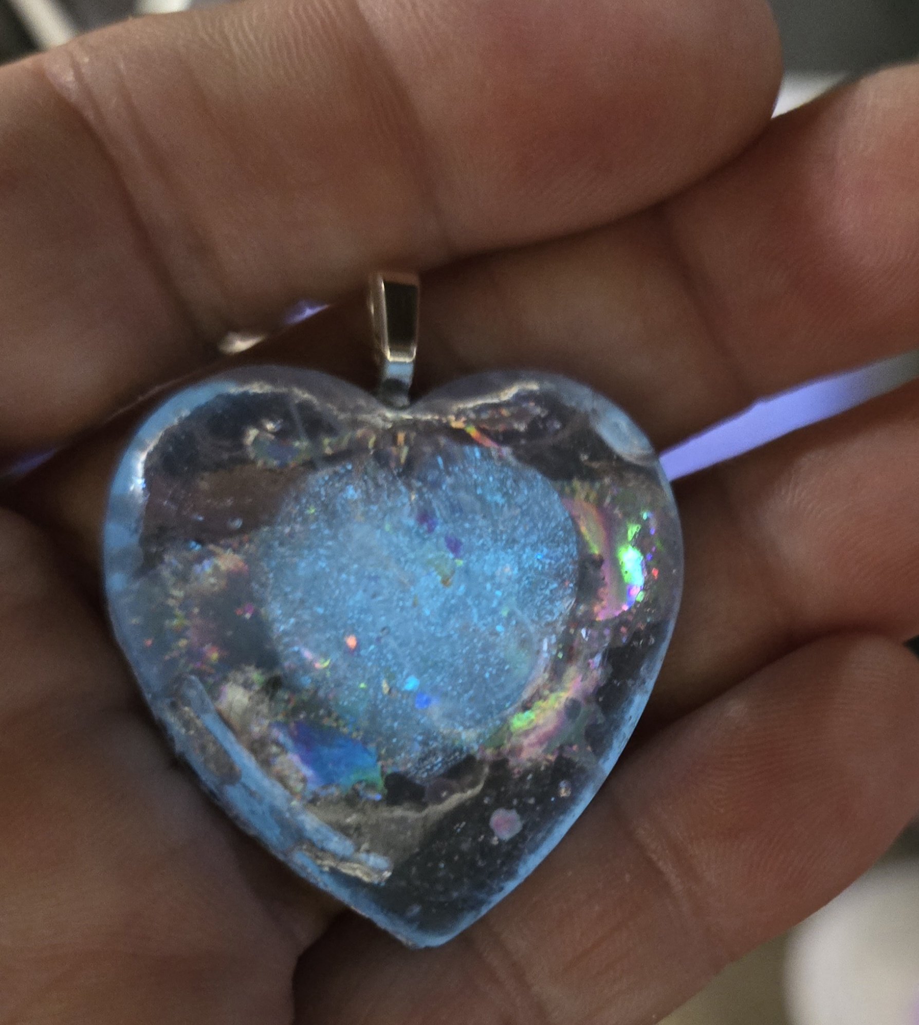 Stock 250 holographic glow heart pendant held in a hand, glowing a soft frosty blue in the center