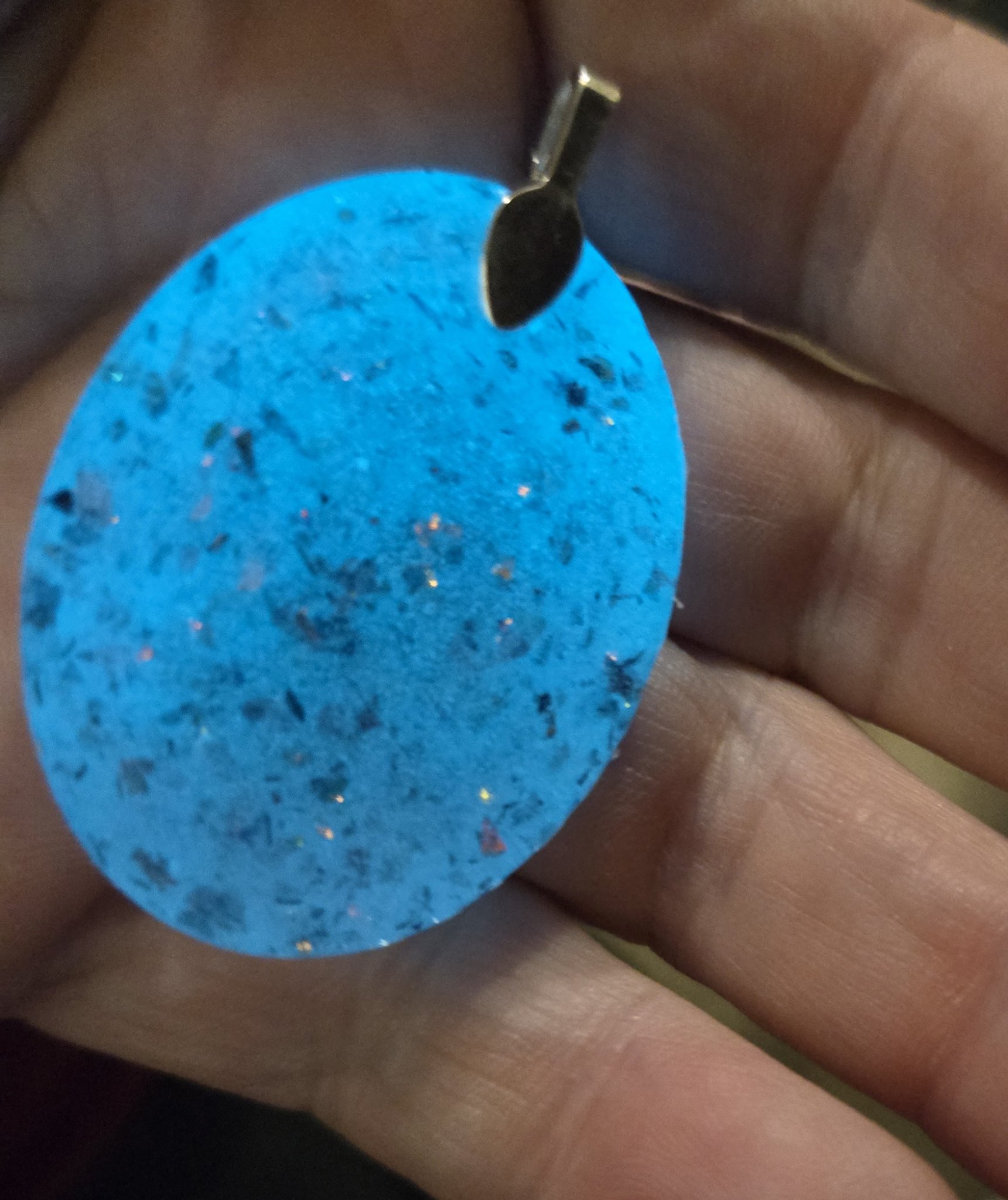 Stock 251 holographic glow oval pendant held in a hand at an angle, glowing bright blue and showing its rounded shape