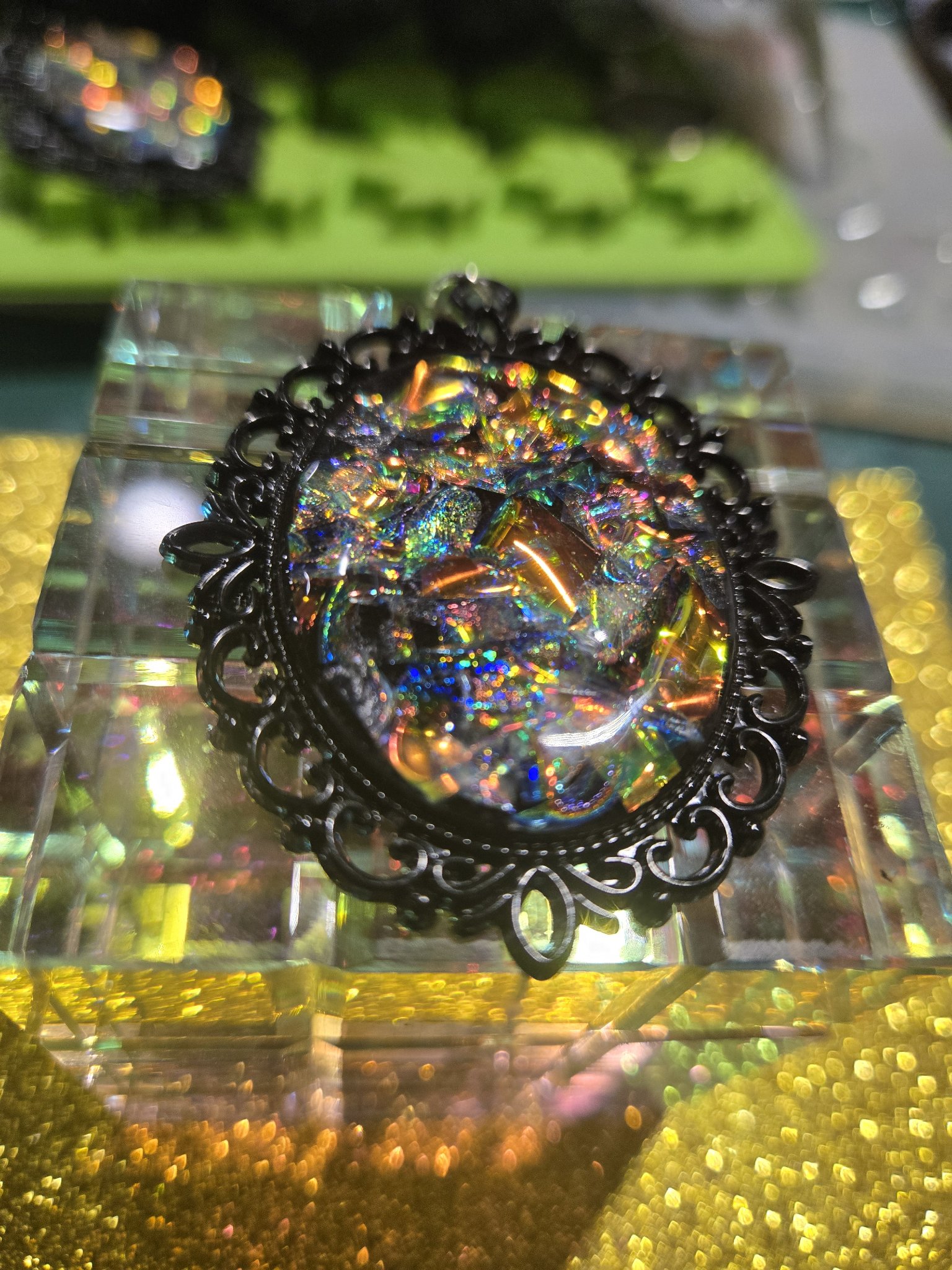 Stock 253 holographic filigree pendant at an angle on a crystal block, showing the domed resin cabochon and the rainbow sparkle of the holographic flakes