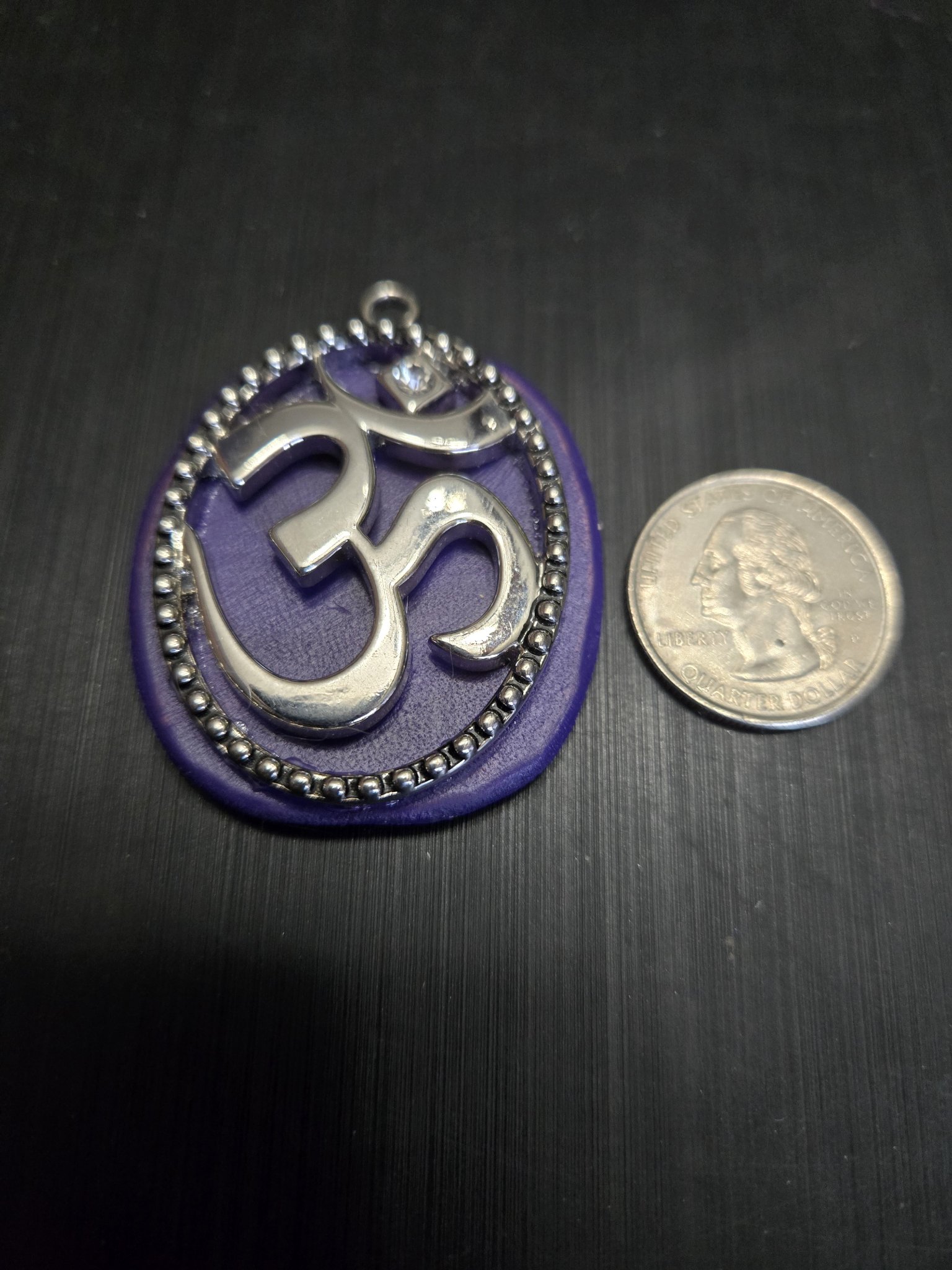 Stock 151 purple leather Om pendant beside a quarter showing it is approximately two and a half inches long