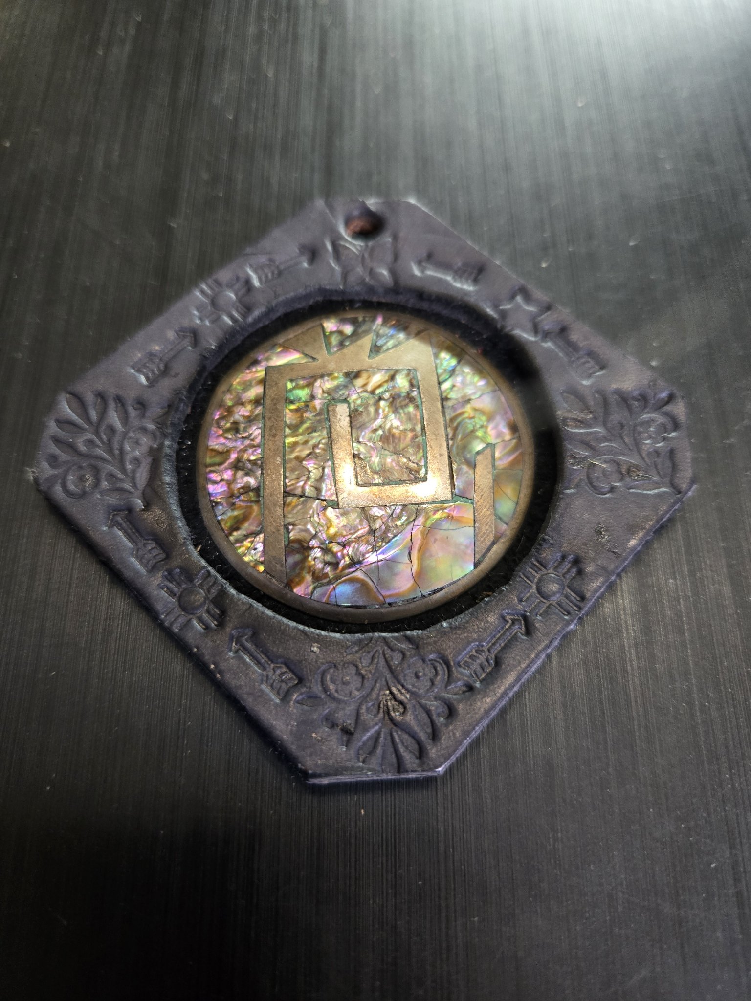 Front close-up of stock 162, a hand-stamped black diamond-shaped leather pendant with a sterling silver and abalone shell center