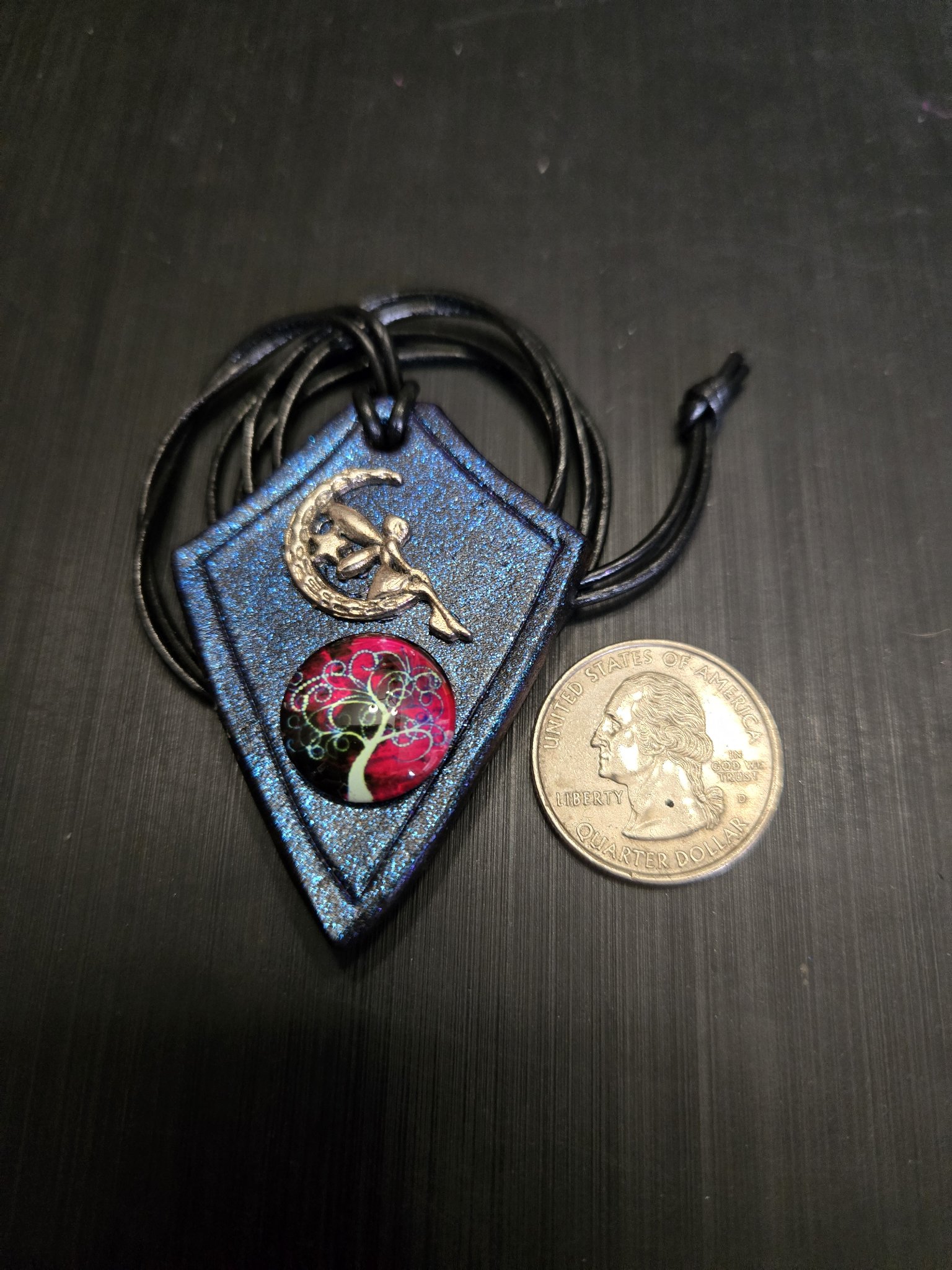 Stock 165 blue iridescent leather fairy moon and tree-of-life pendant beside a quarter for scale