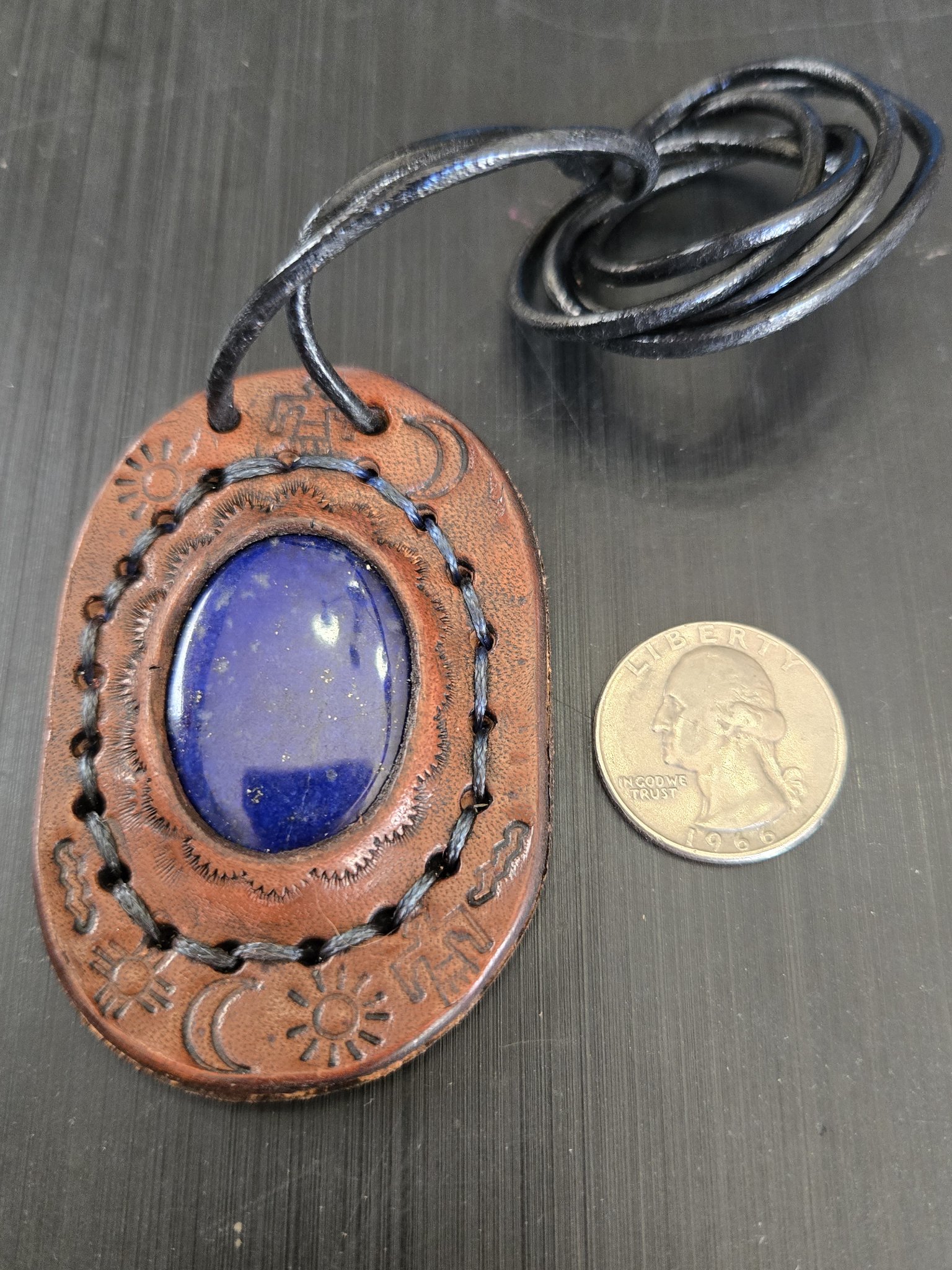 Front of stock 181 hand-sewn lapis leather pendant beside a quarter for scale