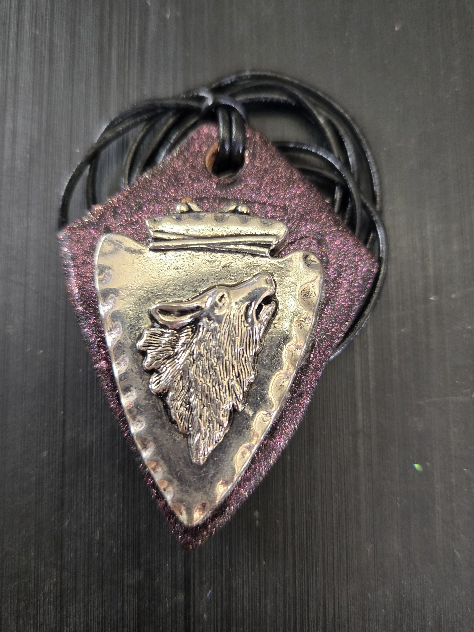 Stock 186 arrowhead-shaped silver-tone metal pendant with a howling wolf head relief on diamond-shaped leather with a pink mica sheen, shown in a front close-up
