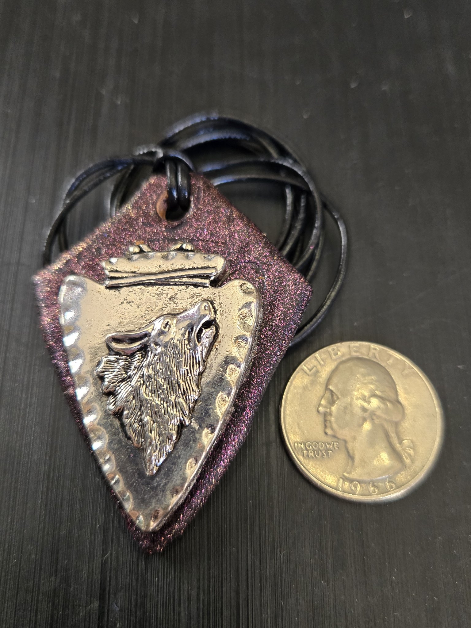 Front of stock 186 wolf arrowhead leather pendant beside a quarter for scale