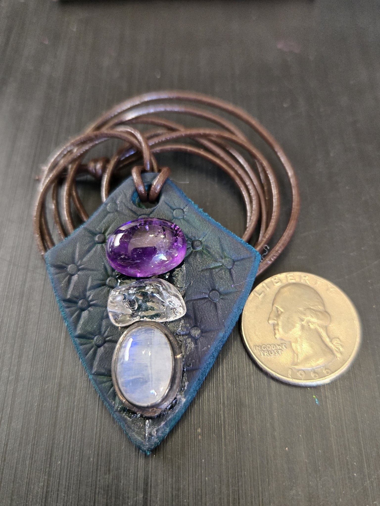 Front of stock 187 three-gemstone dark blue leather pendant beside a quarter for scale