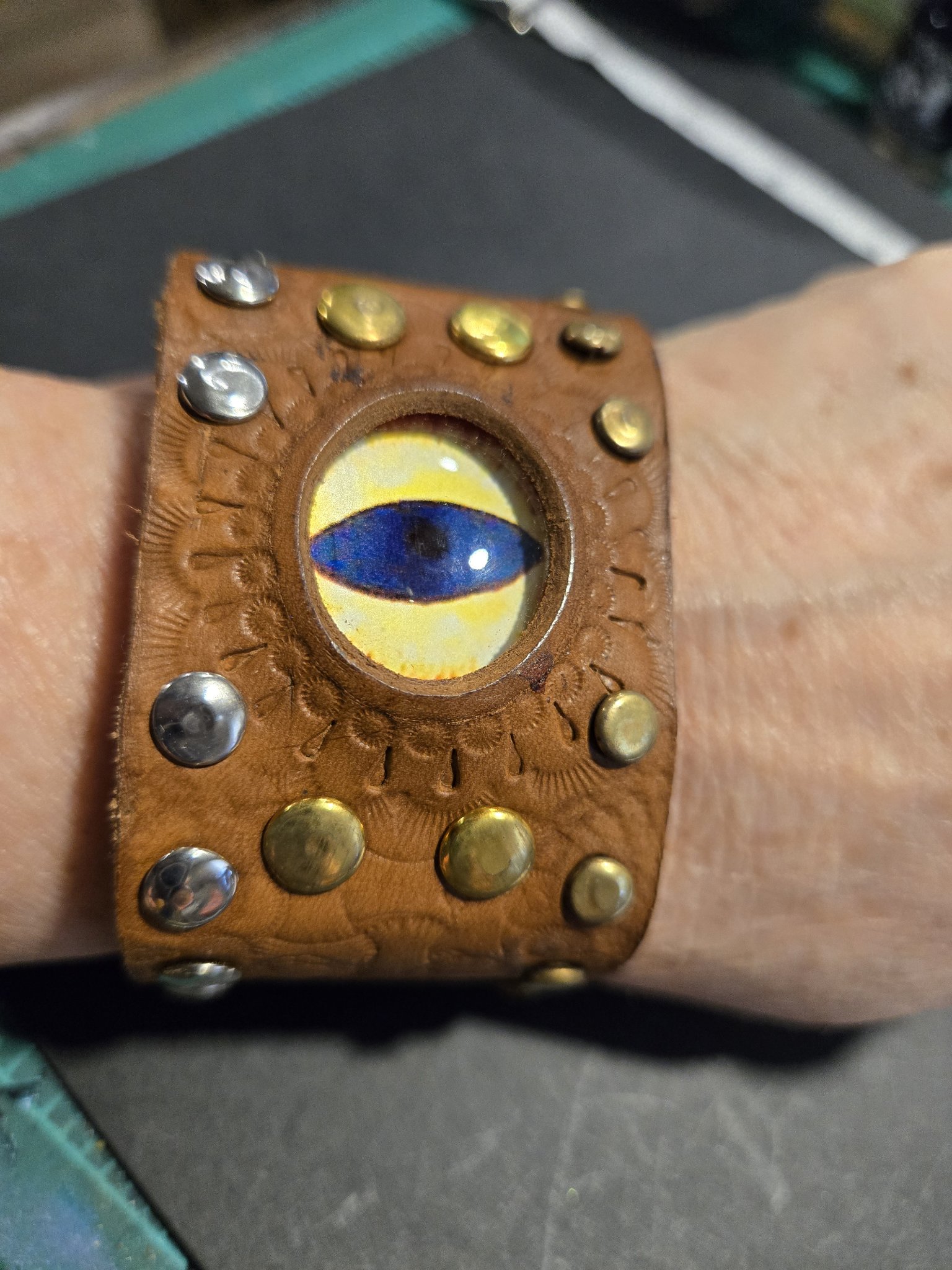 Stock 231 brown leather cuff with a blue and yellow dragon eye ringed with gold and silver tone studs, shown on a wrist